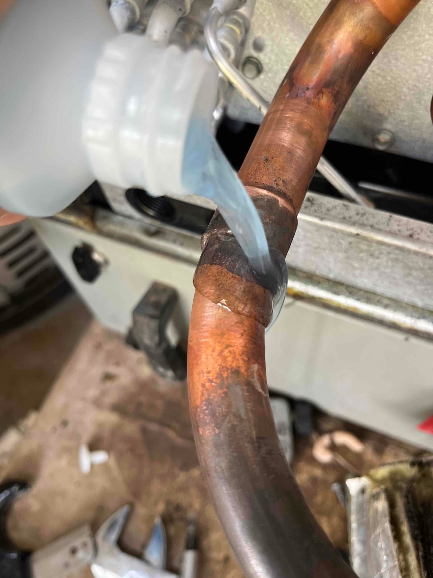 Technician applies leak detection solution to a brazed copper refrigerant line joint to check for leaks after repair.