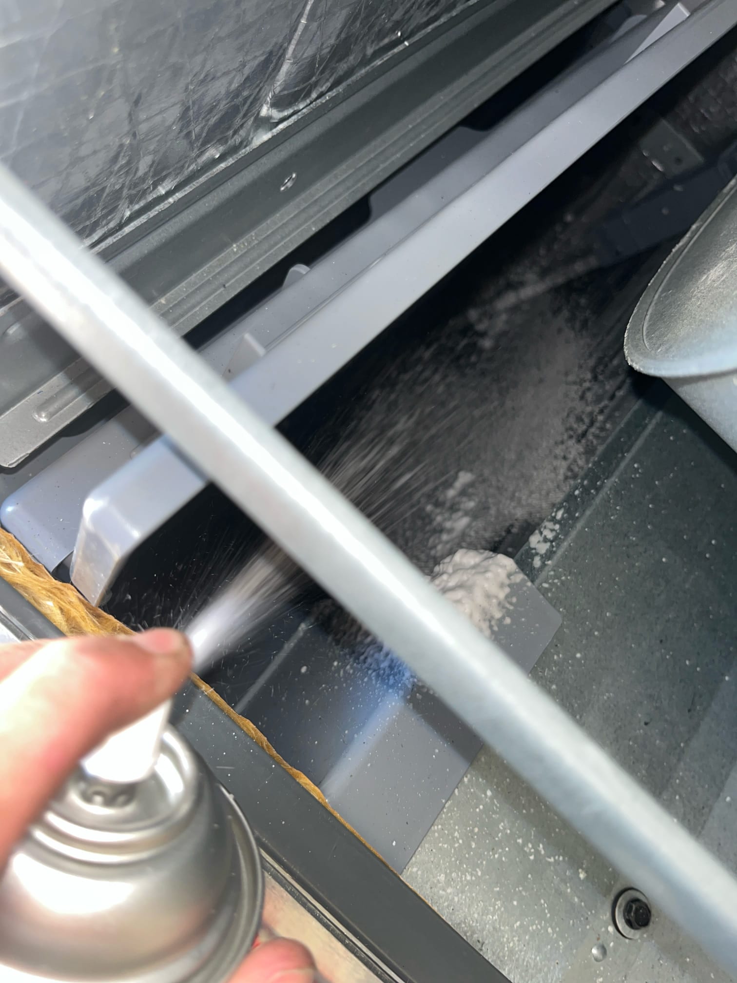Technician sprays cleaner onto an indoor evaporator assembly, coating the coil and drain pan area during service.
