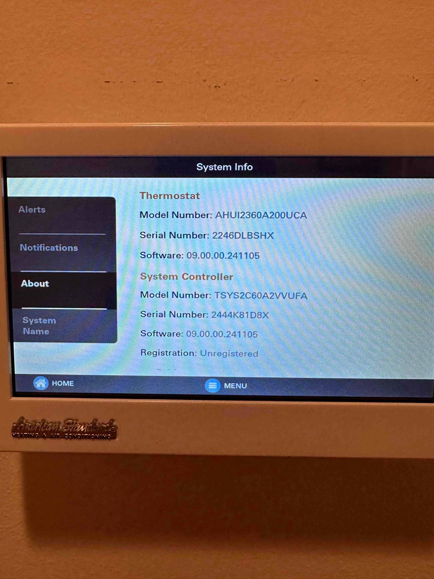 Touchscreen thermostat displays system information menu after installation, showing controller details and registration status on the wall-mounted interface.