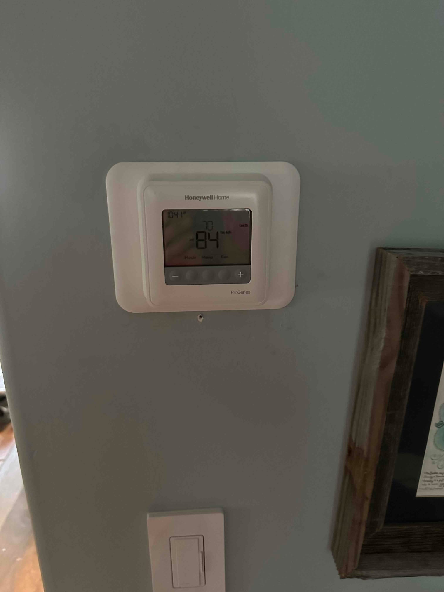 Wall-mounted digital thermostat installed and powered on, displaying indoor temperature and setpoint for the new HVAC system.