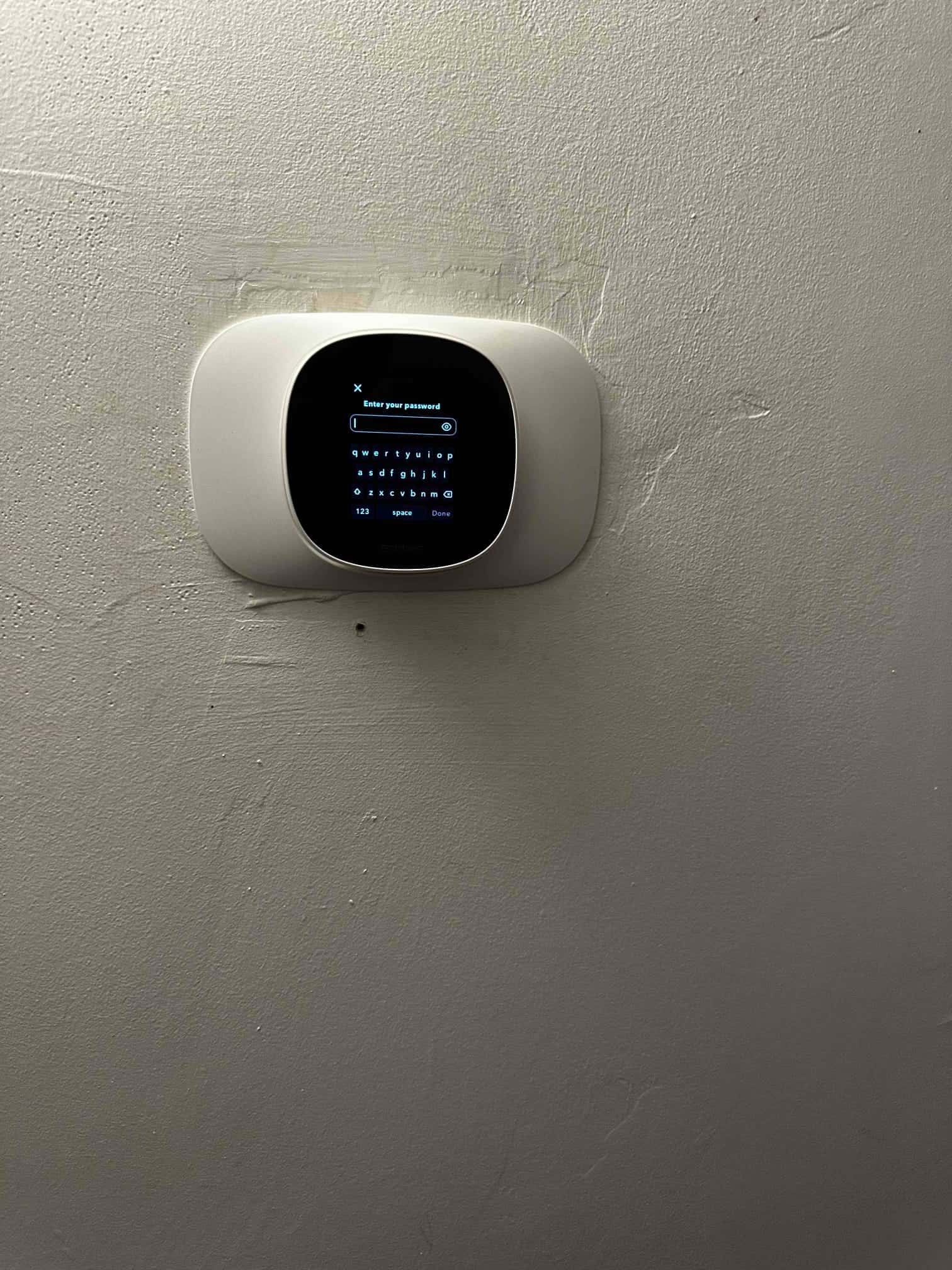 Wall-mounted smart thermostat powered on, displaying an onscreen keyboard for password entry after installation.