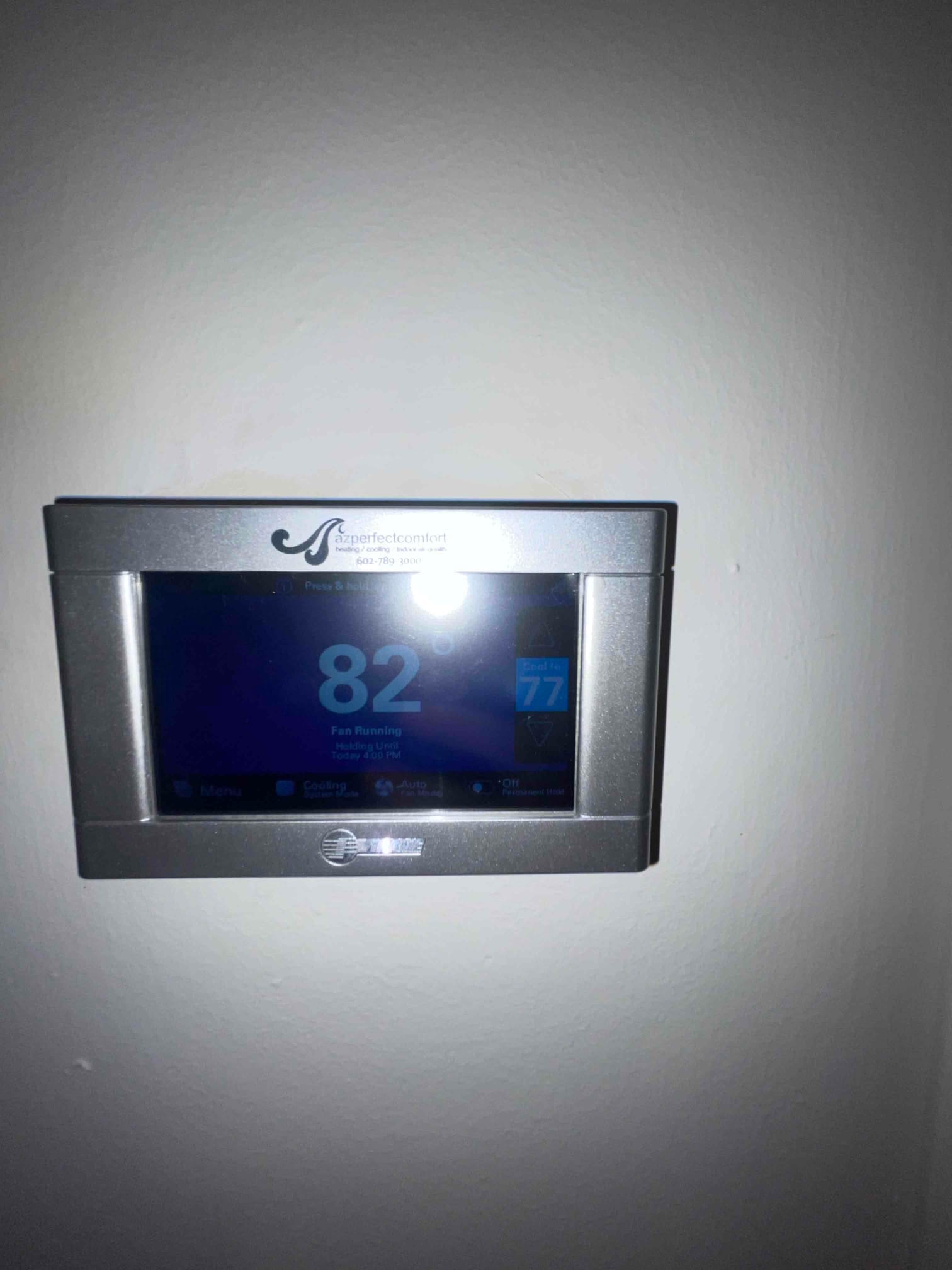 Wall-mounted touchscreen thermostat displays indoor temperature of 82 degrees with a cooling setpoint of 77 degrees.