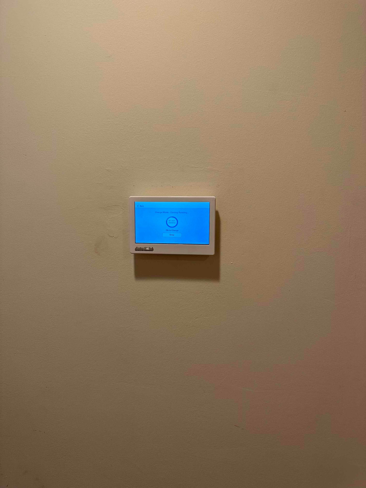 Wall-mounted touchscreen thermostat installed and powered on, showing a cooling mode screen during system setup.