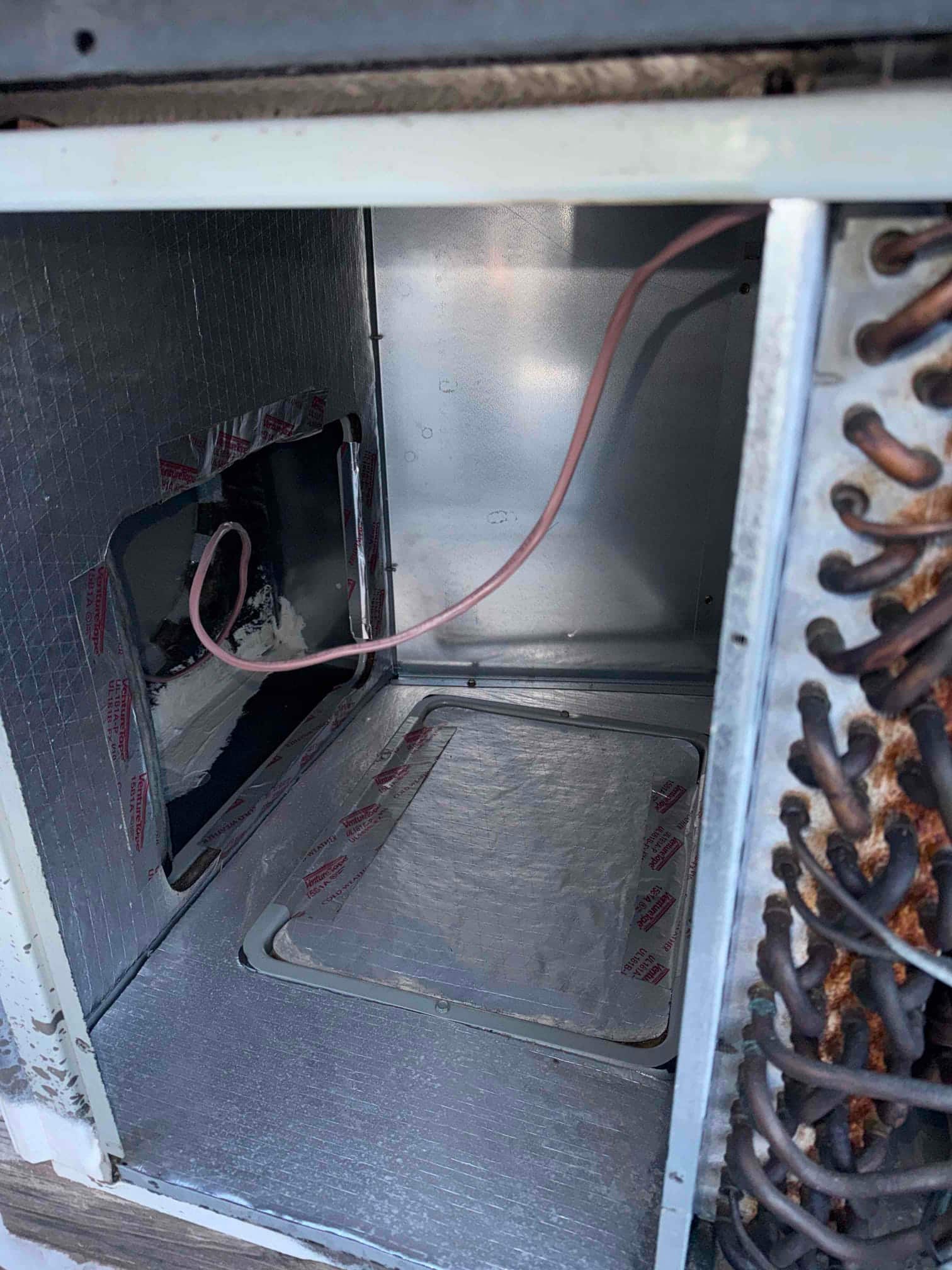 Air handler cabinet interior with new low-voltage thermostat wire routed through the insulated compartment and access panel opening.