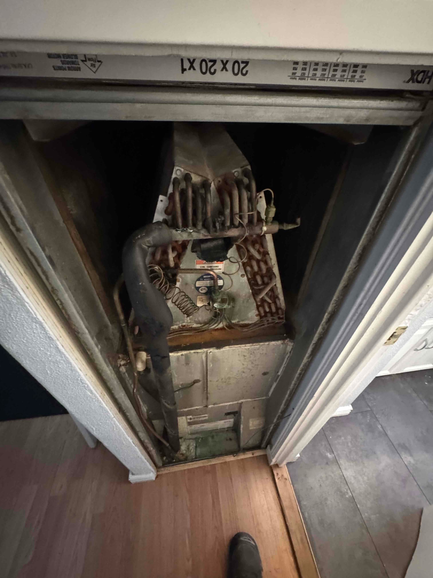 Air handler cabinet open, showing evaporator coil with corrosion, rusted drain pan, and connected refrigerant lines and wiring.