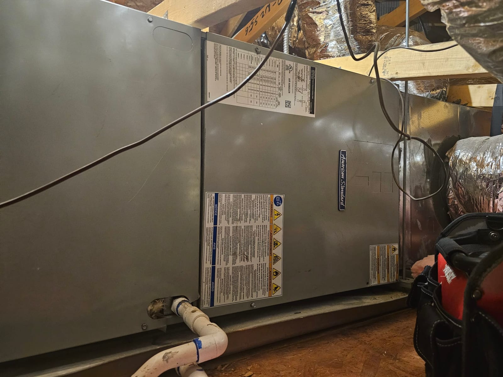 Attic air handler with insulated duct connections and PVC condensate drain line over a drain pan.