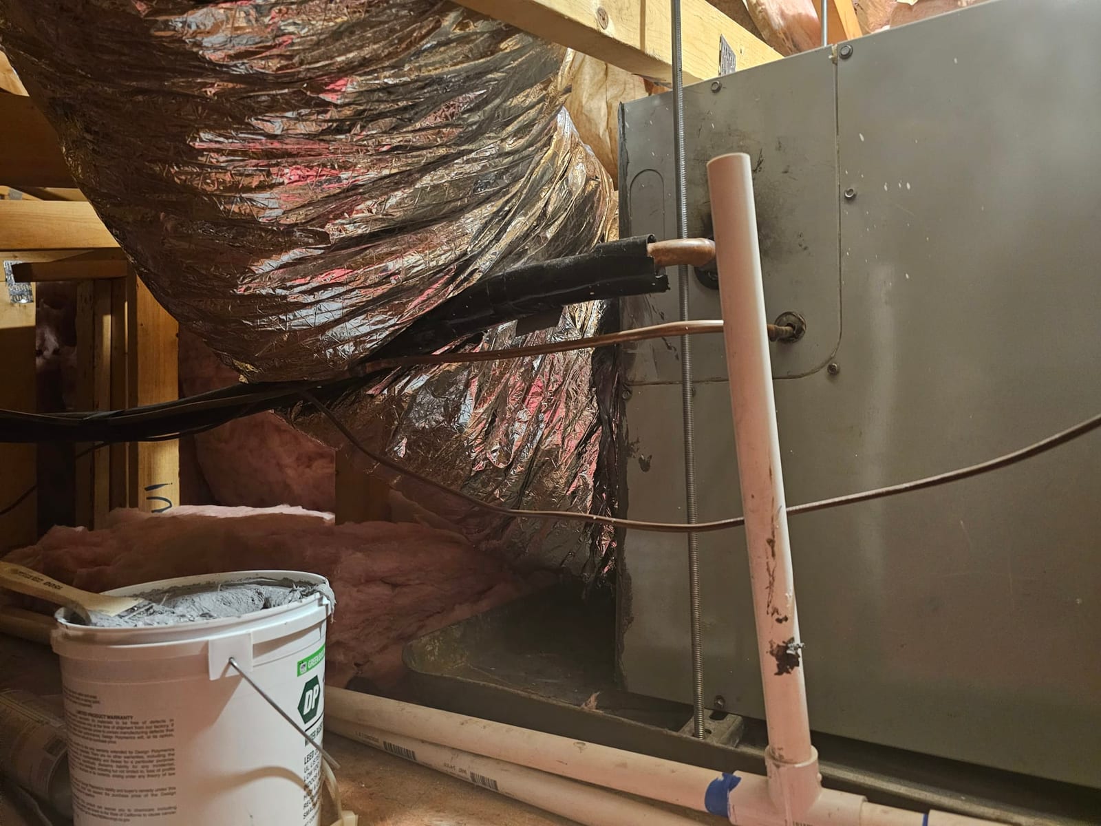 Attic air handler with insulated flex duct connection, copper refrigerant lines, and PVC condensate drain piping visible.