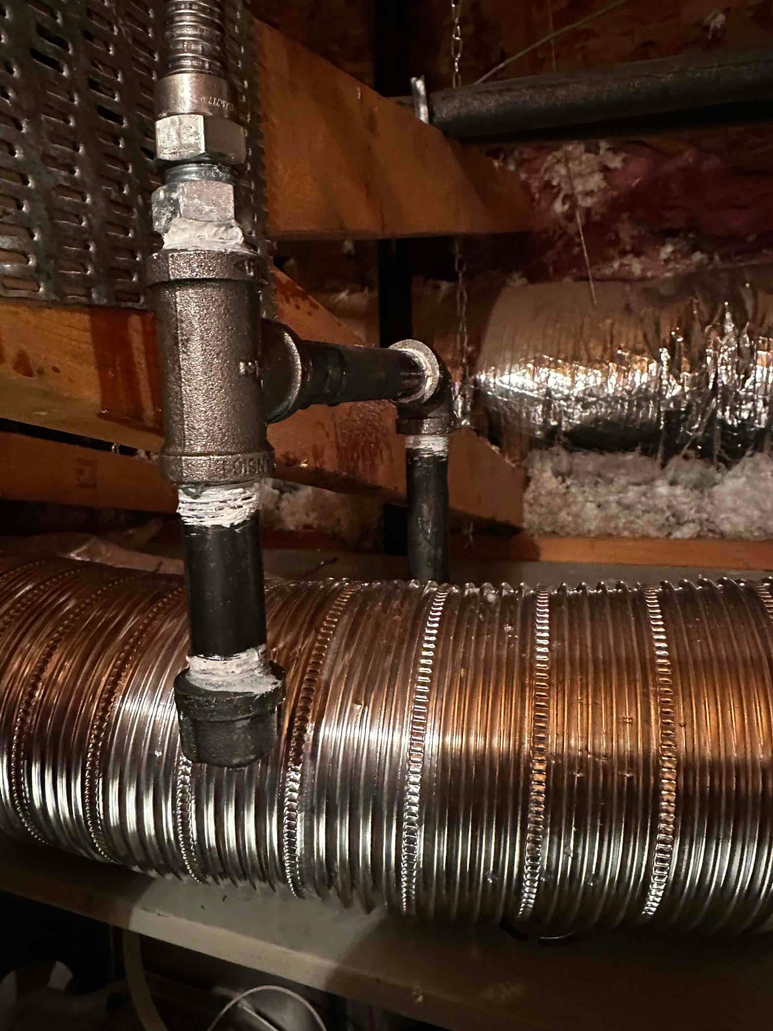 Black iron gas piping with fittings and sealant routed above spiral metal duct in the attic space.
