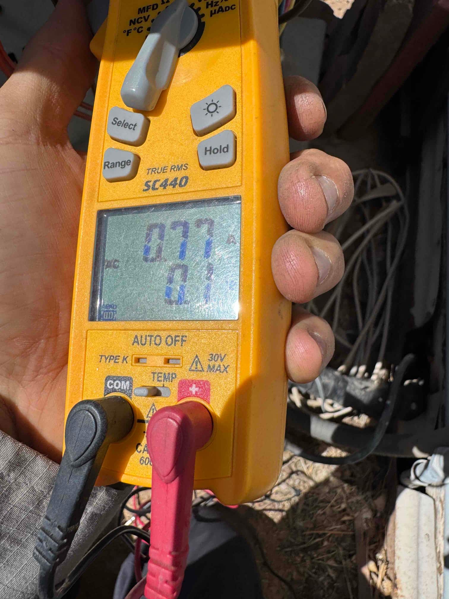 Clamp meter display shows 0.77 A with test leads connected at the HVAC unit wiring compartment.