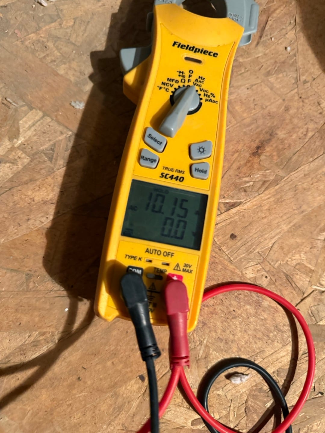 Clamp meter display shows 10.15 A with test leads connected, measuring current during HVAC system diagnostics.