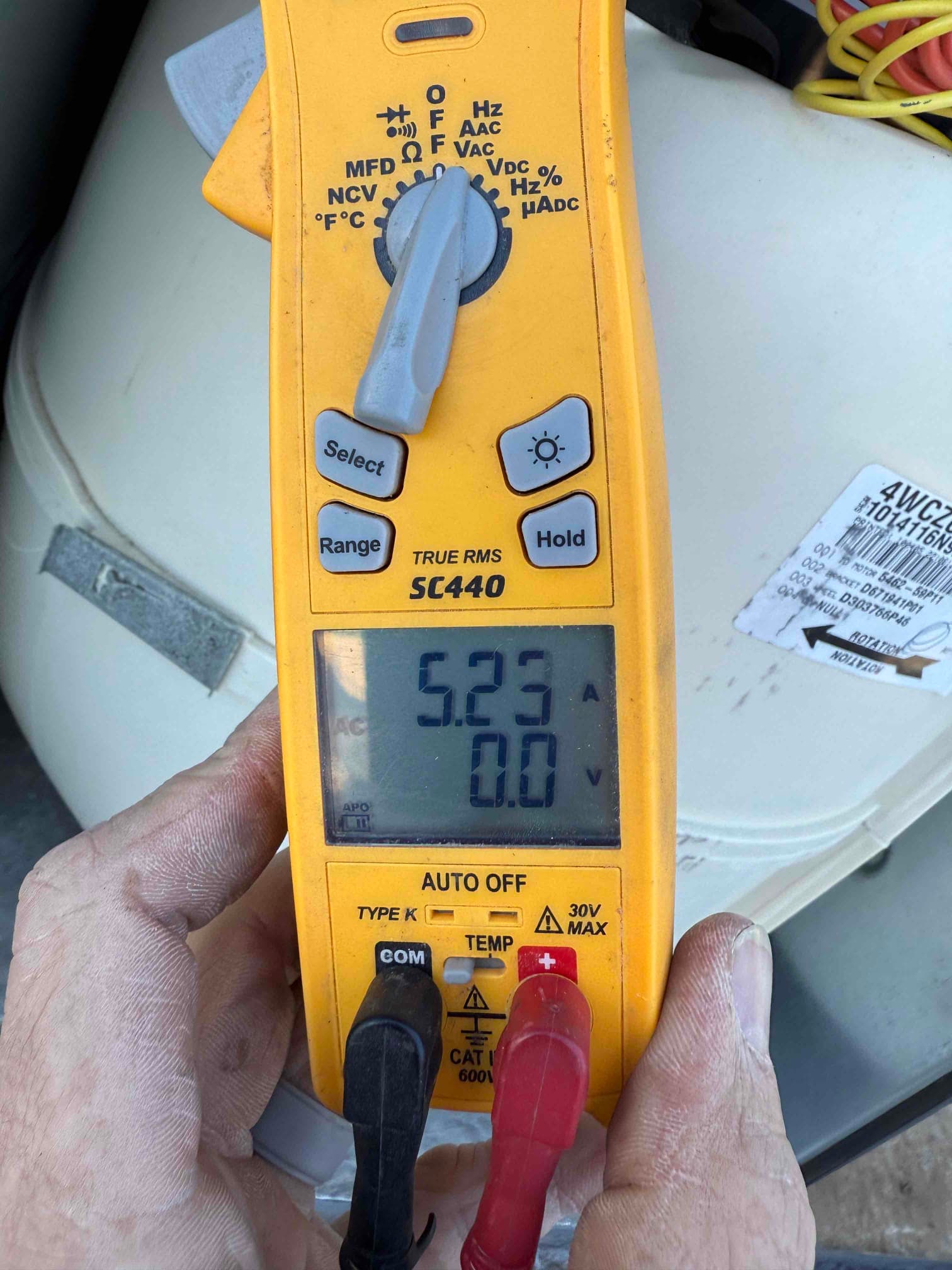 Clamp meter display shows 5.23 A on the clamped conductor, with test leads connected and HVAC equipment in background.