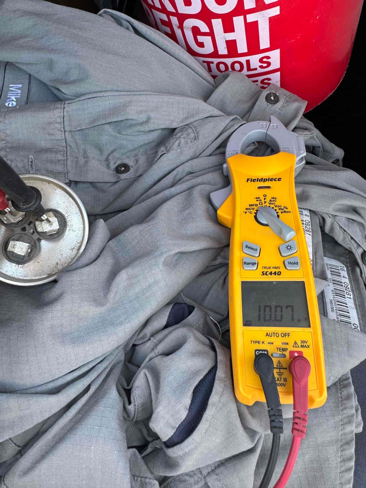Clamp meter displays 10.87 A with the jaw clamped on a conductor during HVAC diagnostic testing.