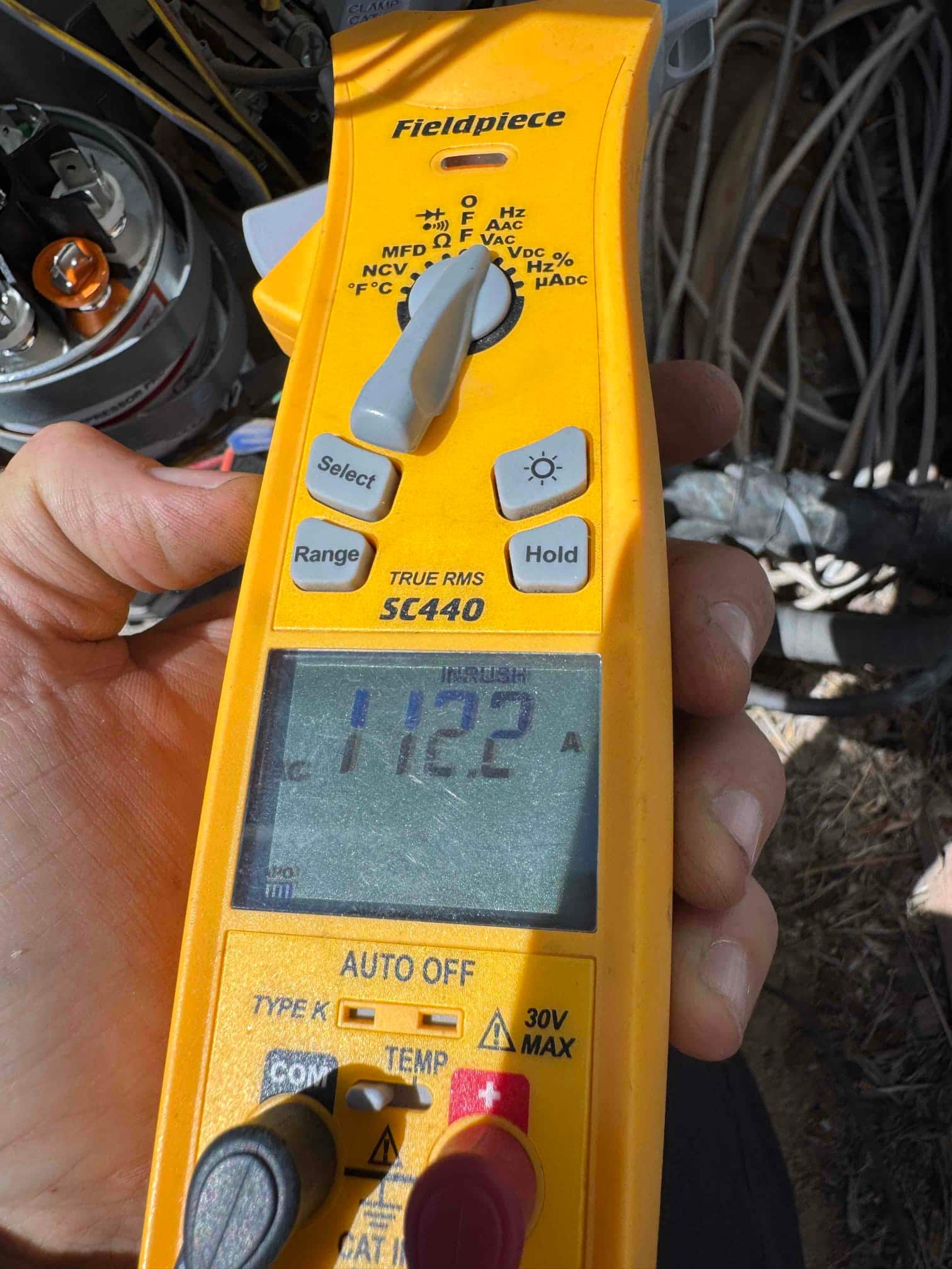 Clamp meter shows 11.22 A on a single conductor near the outdoor unit during air conditioning repair.