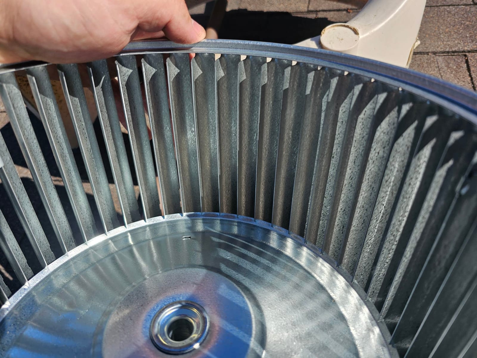 Clean metal blower wheel removed from the air handler, showing intact fins and hub with technician’s hand holding the rim.