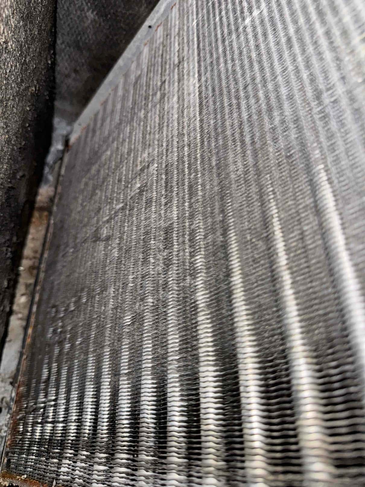 Close-up of an HVAC evaporator coil surface with aluminum fins, showing accumulated dust and debris between the fin channels.
