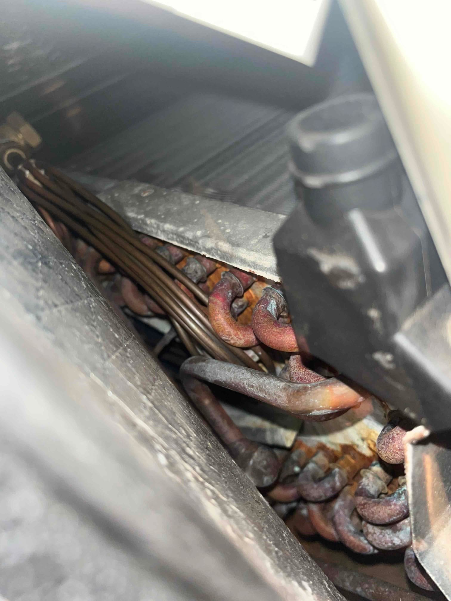 Close-up of indoor evaporator coil and copper refrigerant tubing with visible rust and corrosion on multiple bends.