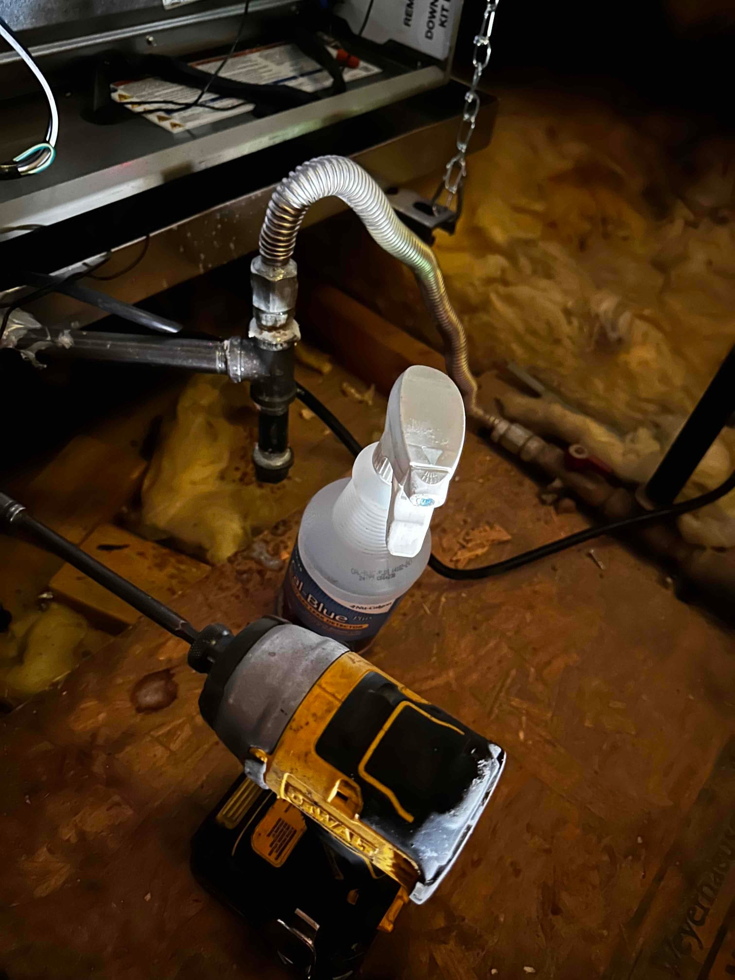 Condensate drain assembly beneath an indoor air handler with new fittings and cleaning spray bottle positioned on the attic floor.