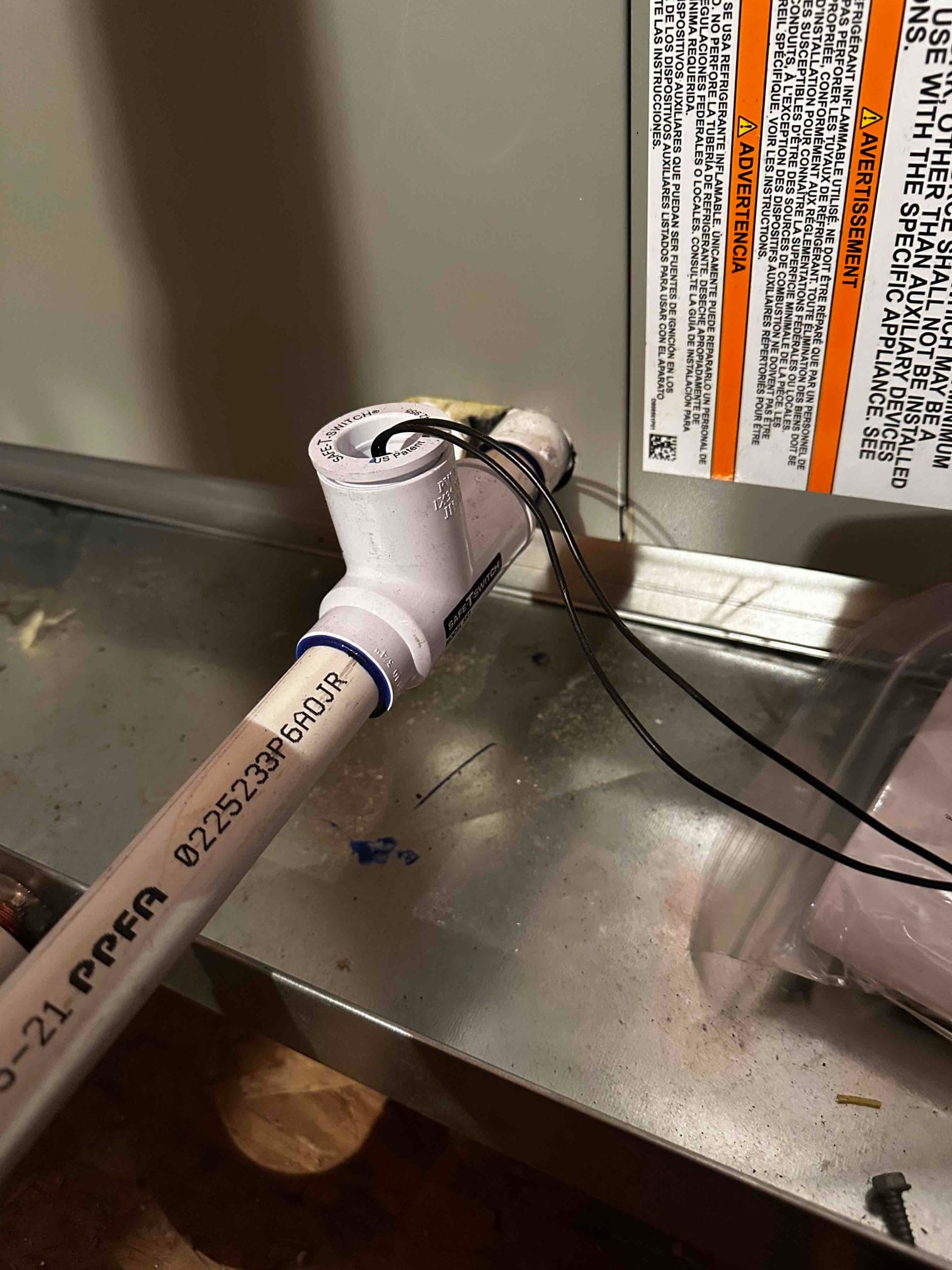 Condensate drain assembly installed at the air handler with a T-fitting and float switch wiring routed through the cleanout cap.