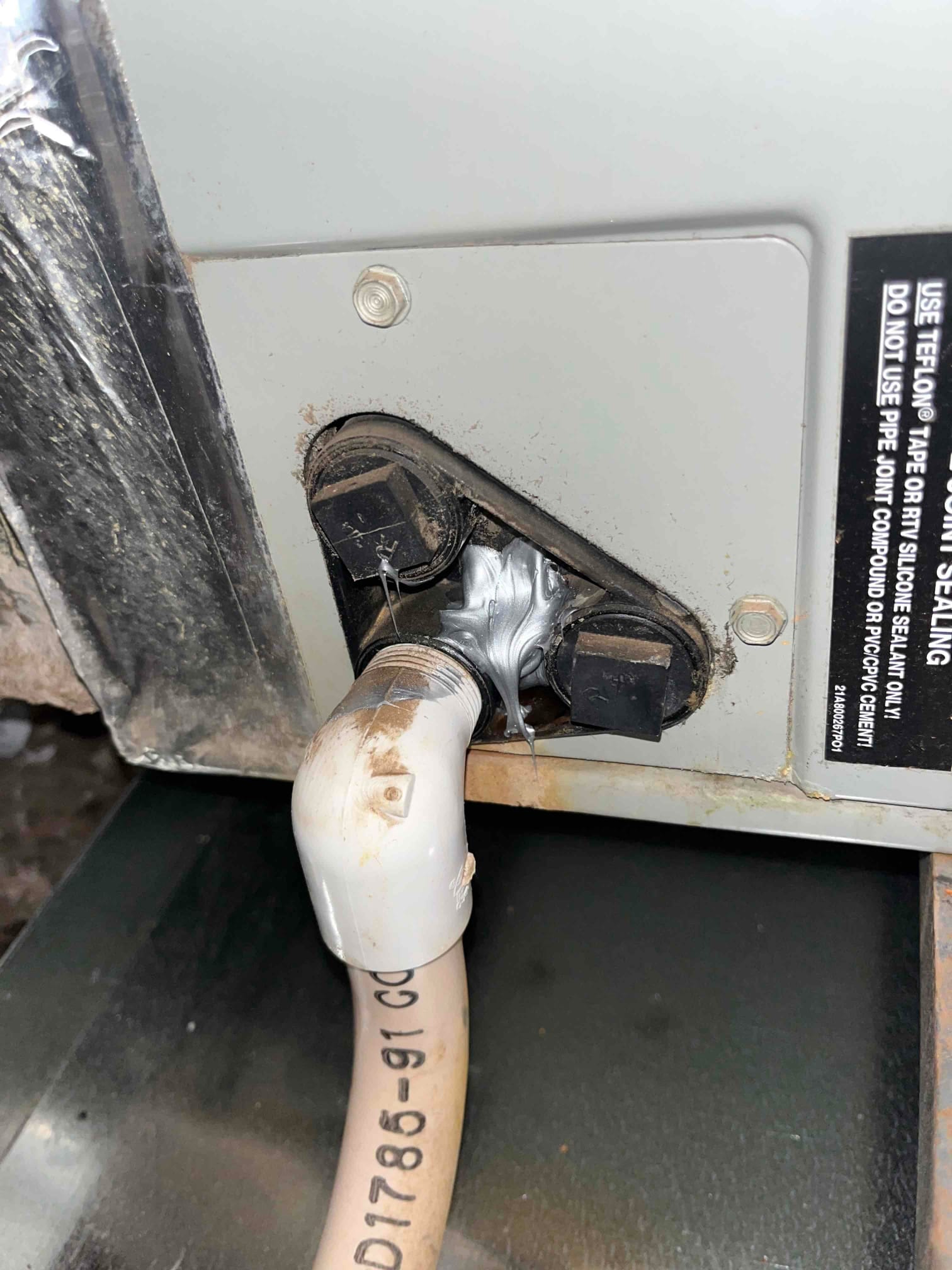 Condensate drain connection at the air handler, showing new PVC elbow and fresh sealant applied around the drain port.