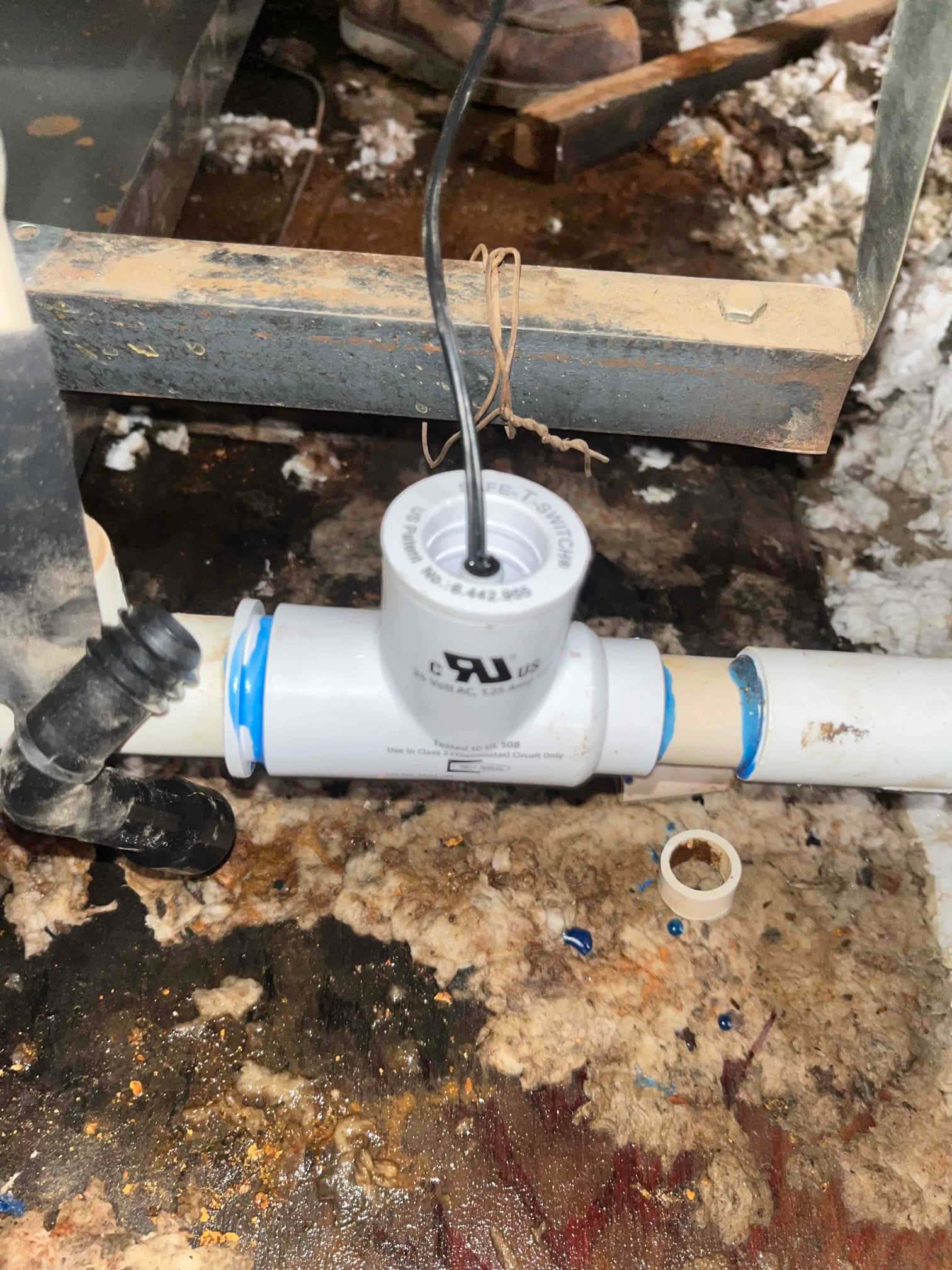 Condensate drain line with an inline float safety switch installed above insulation debris near the air handler base.