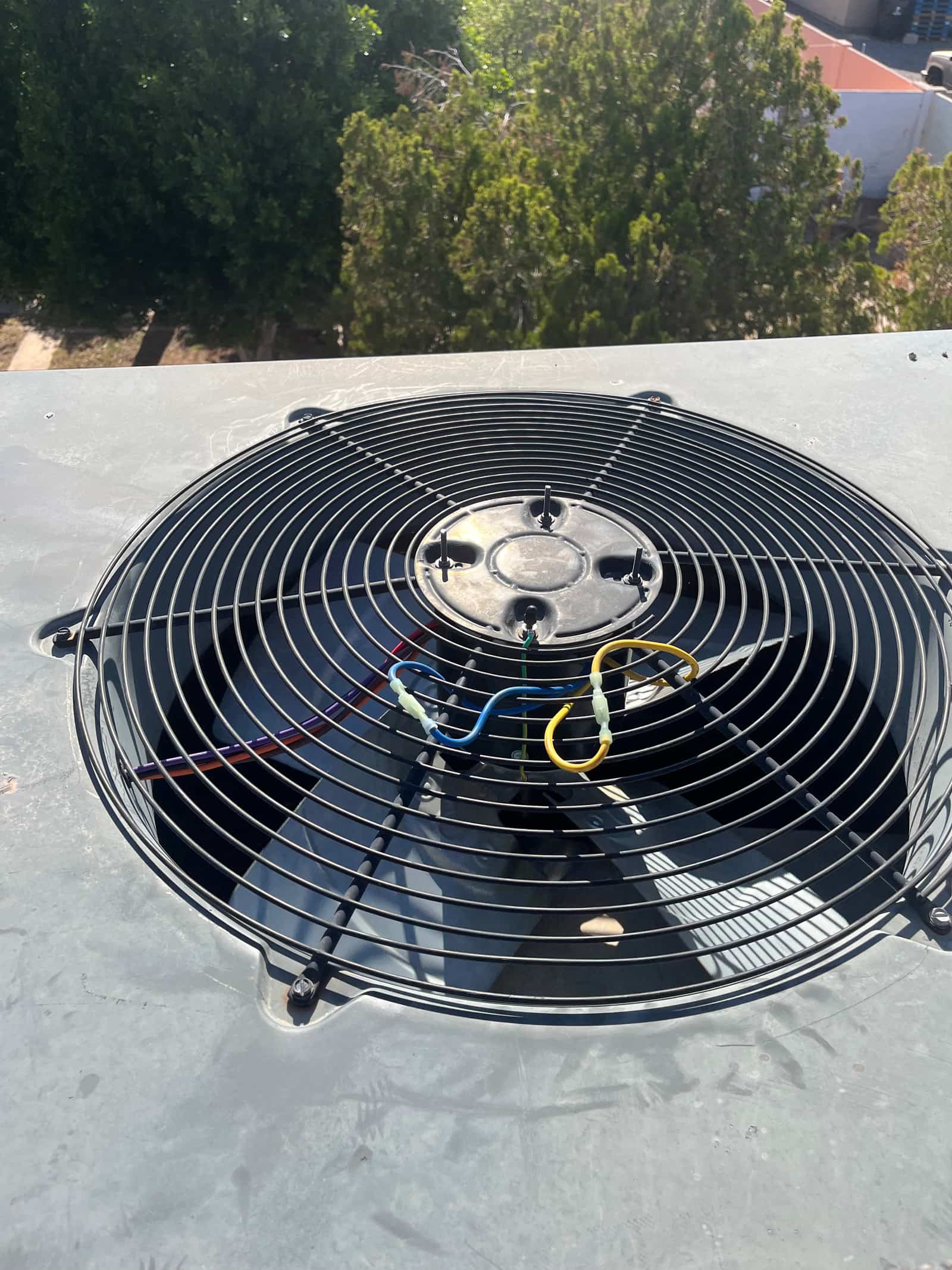 Condenser fan assembly on rooftop unit, showing protective grille and exposed fan motor wiring routed through the center hub.