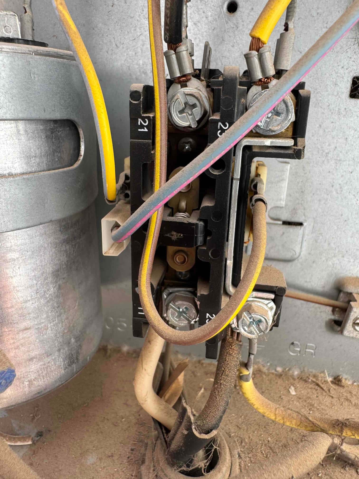 Contactor with connected wiring inside an outdoor condenser compartment, adjacent to a cylindrical capacitor, showing dust buildup on components.