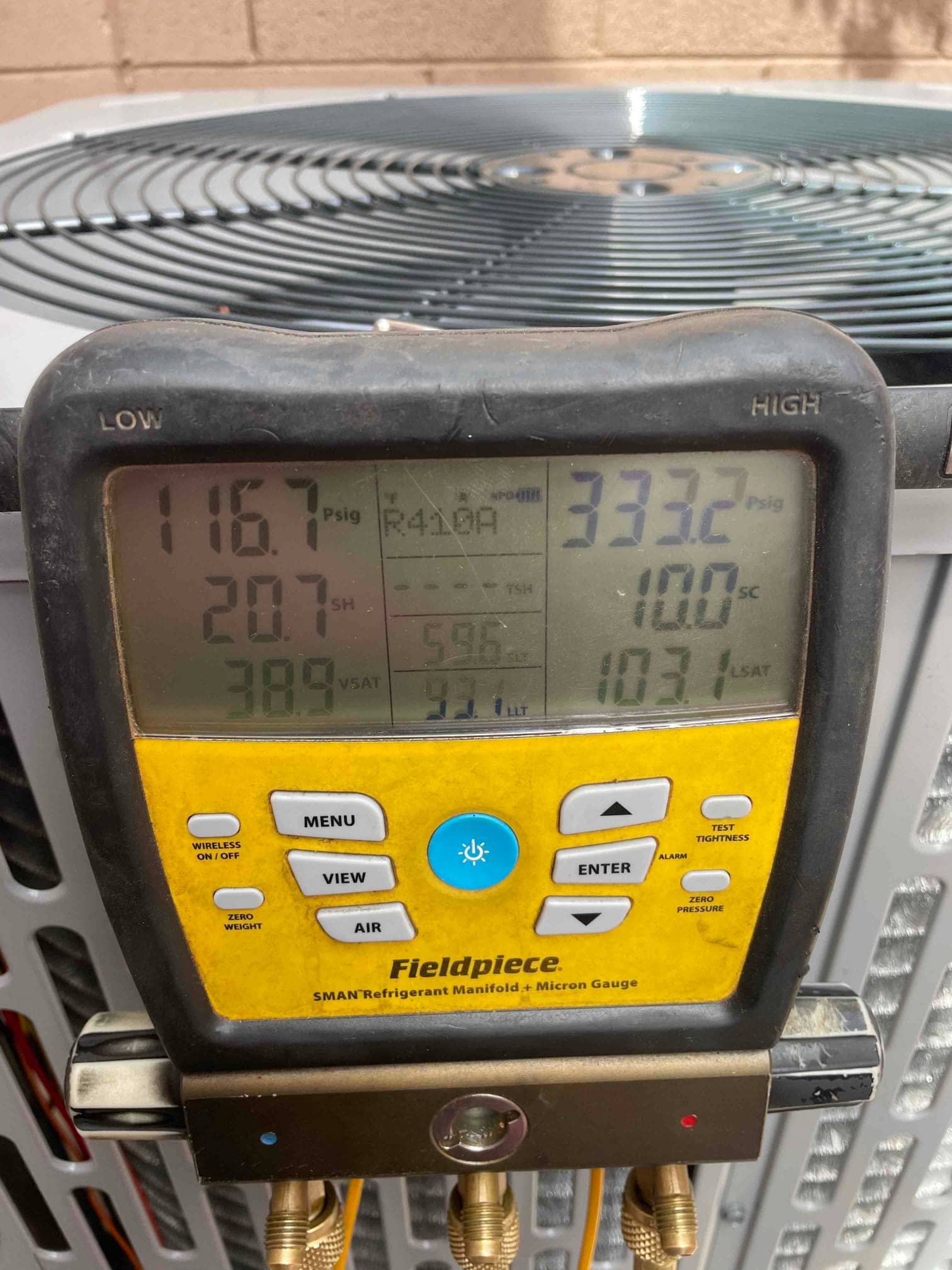 Digital manifold connected at the outdoor unit shows operating pressures and calculated subcooling and superheat during system commissioning.