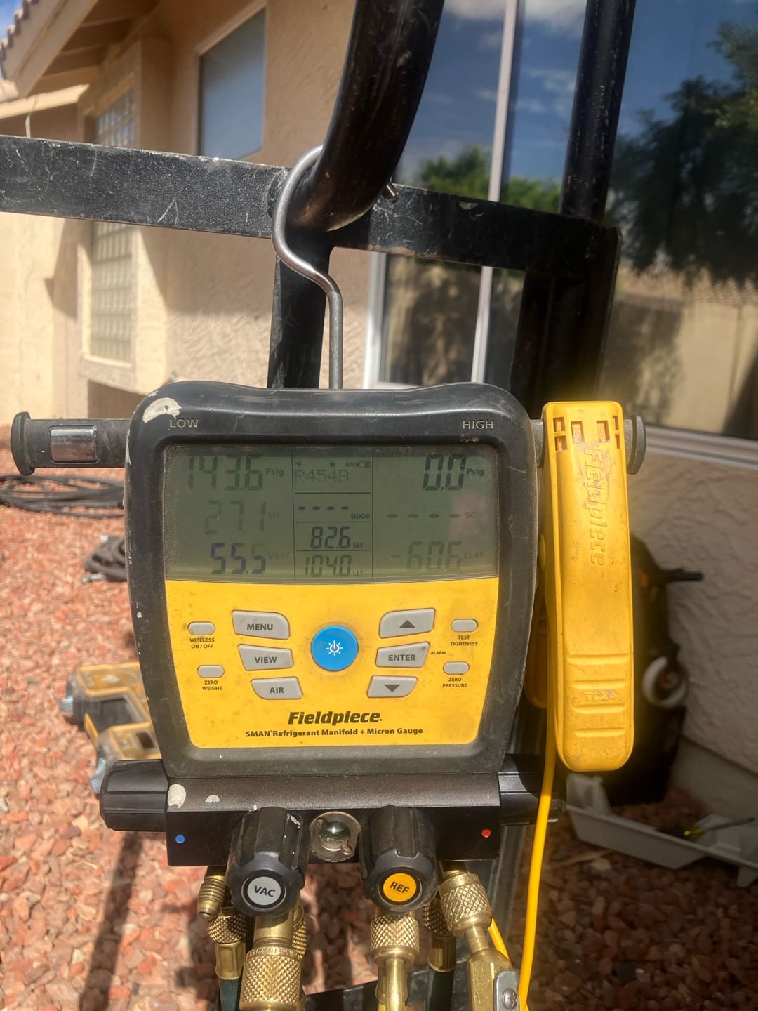 Digital manifold connected to the system shows operating pressures and temperatures during refrigerant commissioning outside the home.