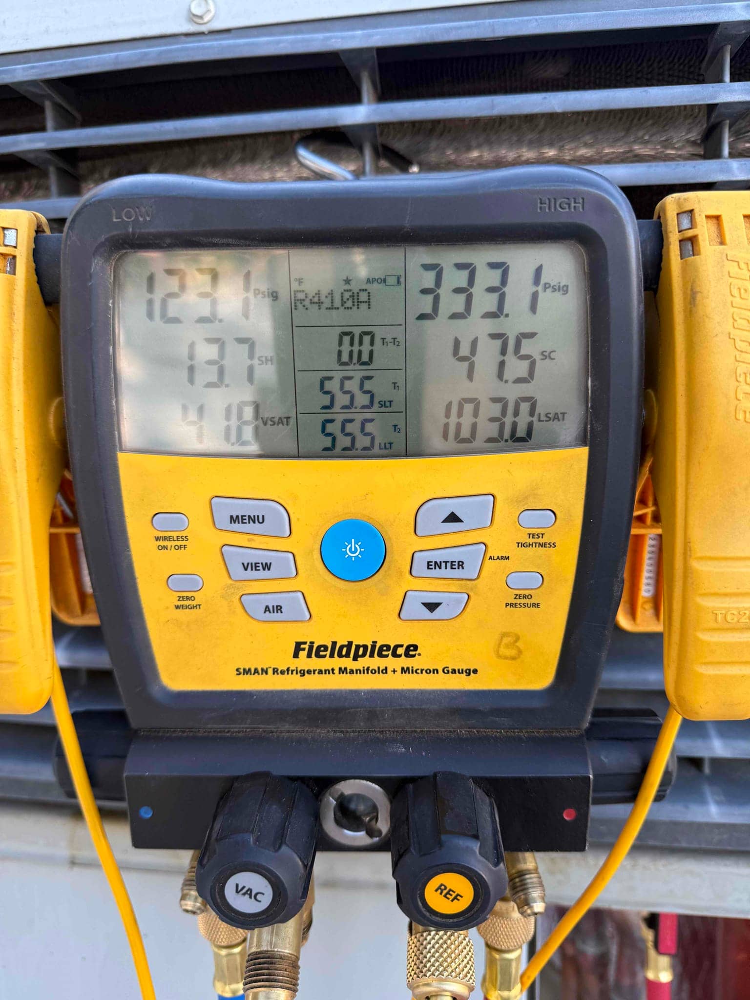 Digital manifold gauge on an outdoor condenser shows high-side pressure at 555 psi while measuring R410A system pressures and temperatures.