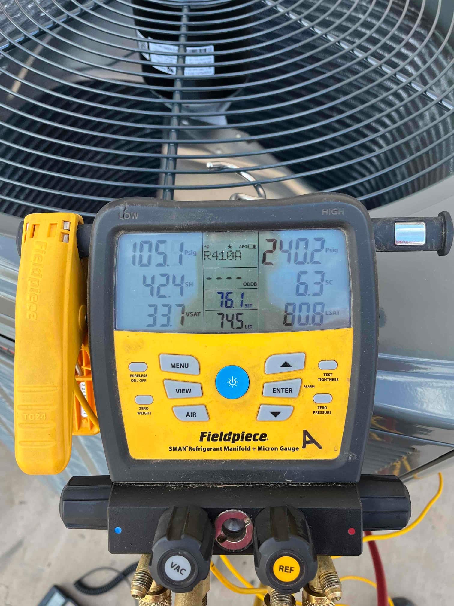 Digital manifold gauges show system operating pressures while connected at the outdoor condenser during commissioning.