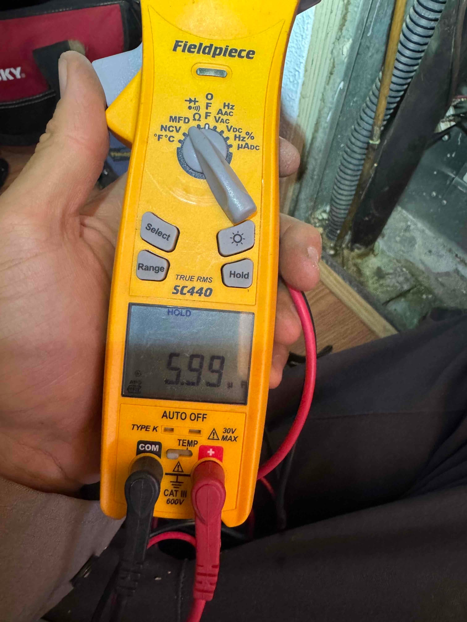 Digital multimeter set to capacitance shows 5.99 μF while measuring a capacitor with red and black leads connected.