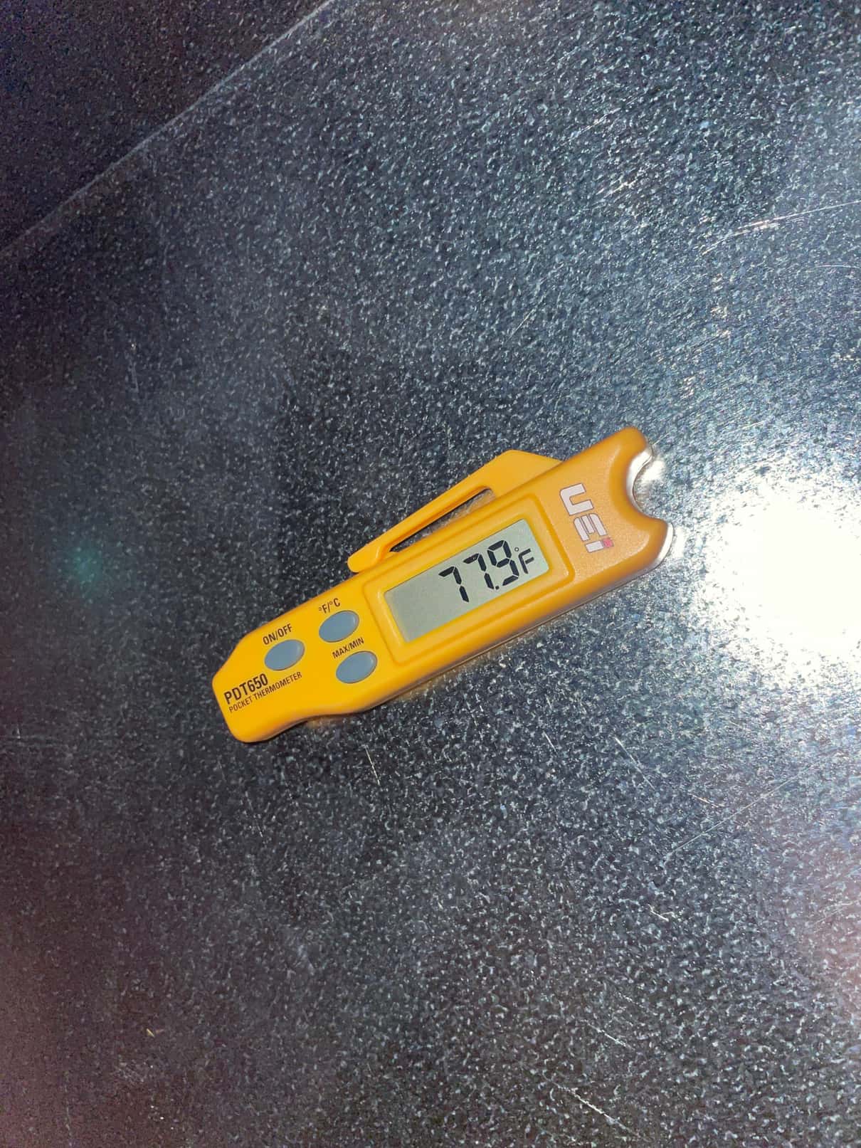 Digital pocket thermometer displays 77.9°F while measuring air temperature on a metal HVAC surface during commissioning.
