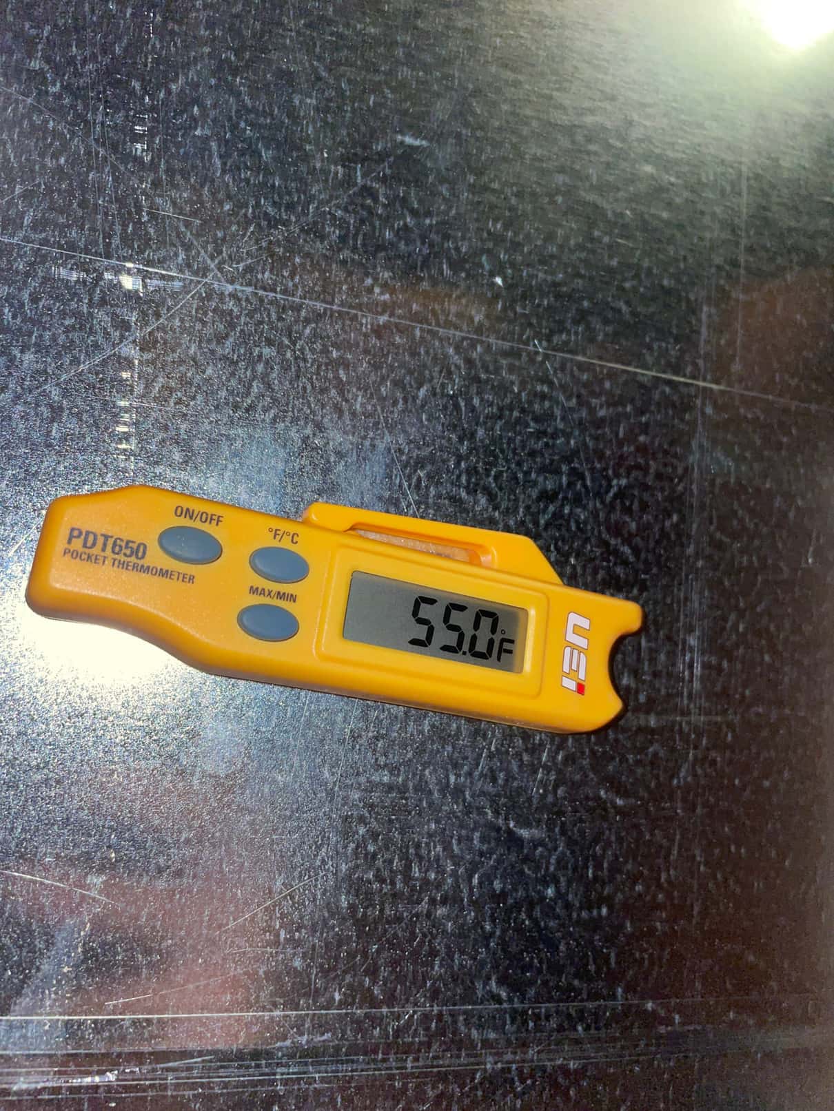 Digital pocket thermometer shows 55.0°F on the duct surface, documenting cool supply air during system commissioning.