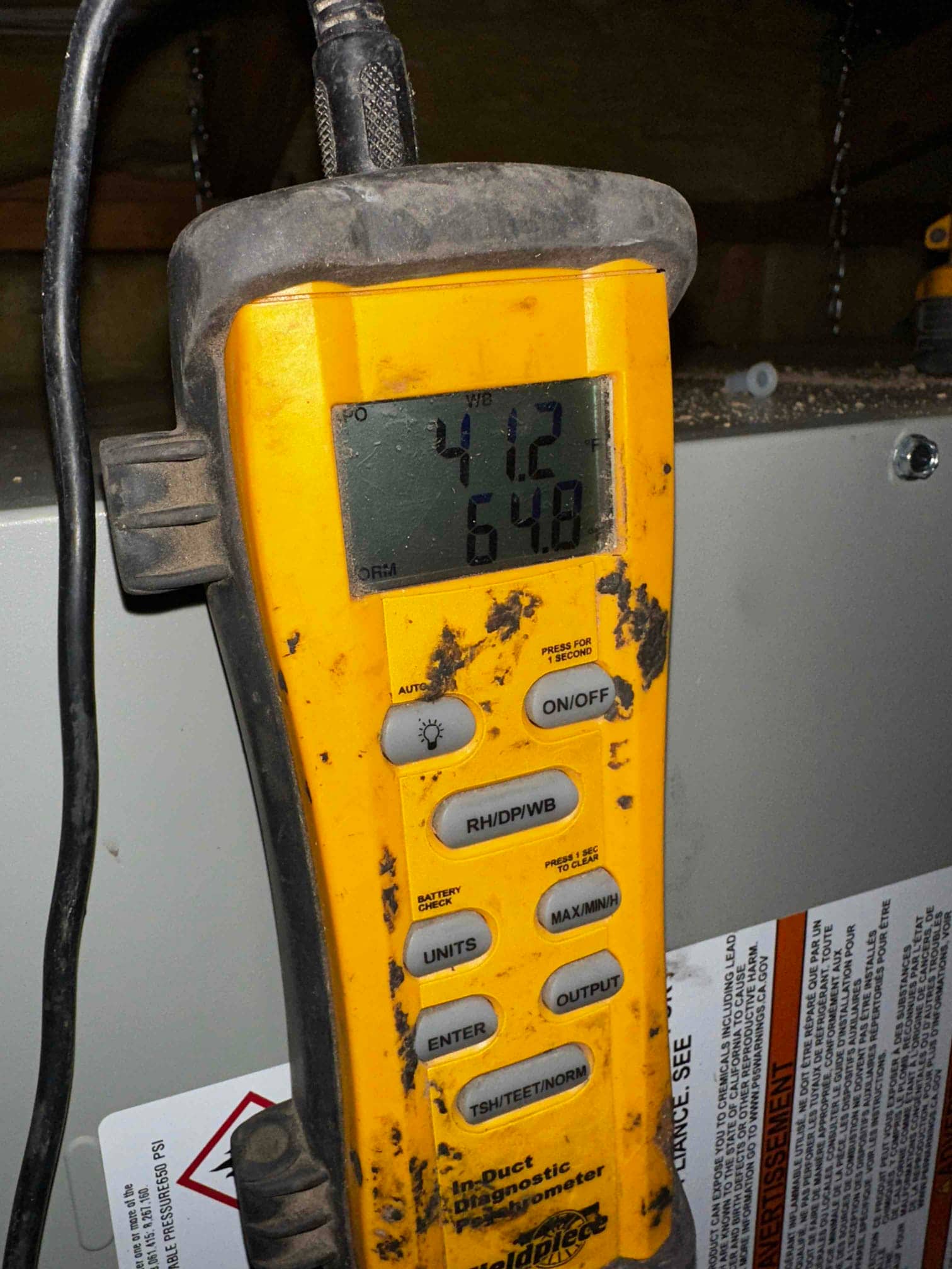 Digital probe thermometer shows 64.8°F in-duct air temperature during commissioning near the indoor unit cabinet.