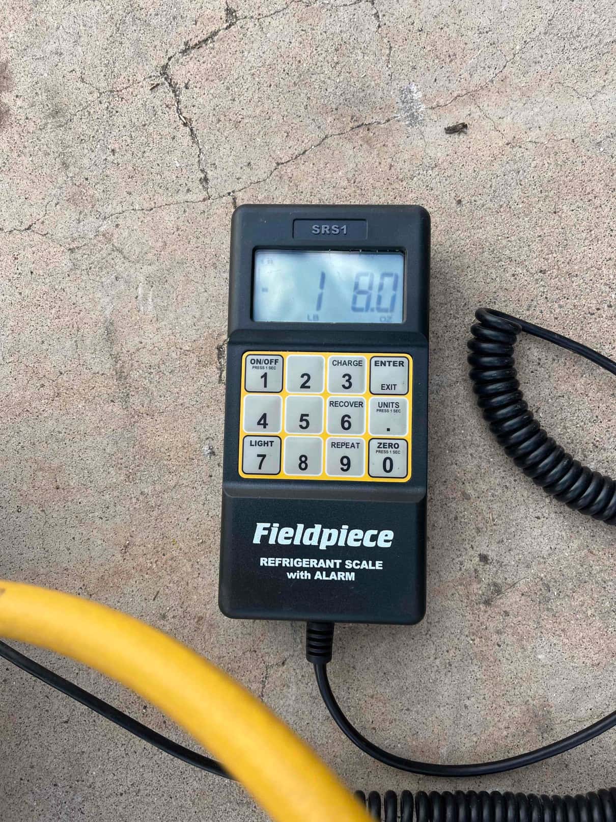 Digital refrigerant scale handheld display on the job site shows 1 lb 8 oz during charging work.