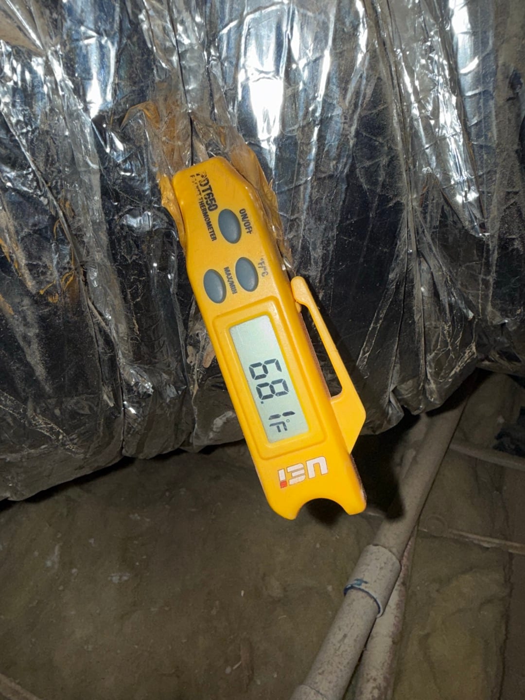 Digital thermometer clipped to insulated duct shows 68.8 °F on the display during air conditioning repair.