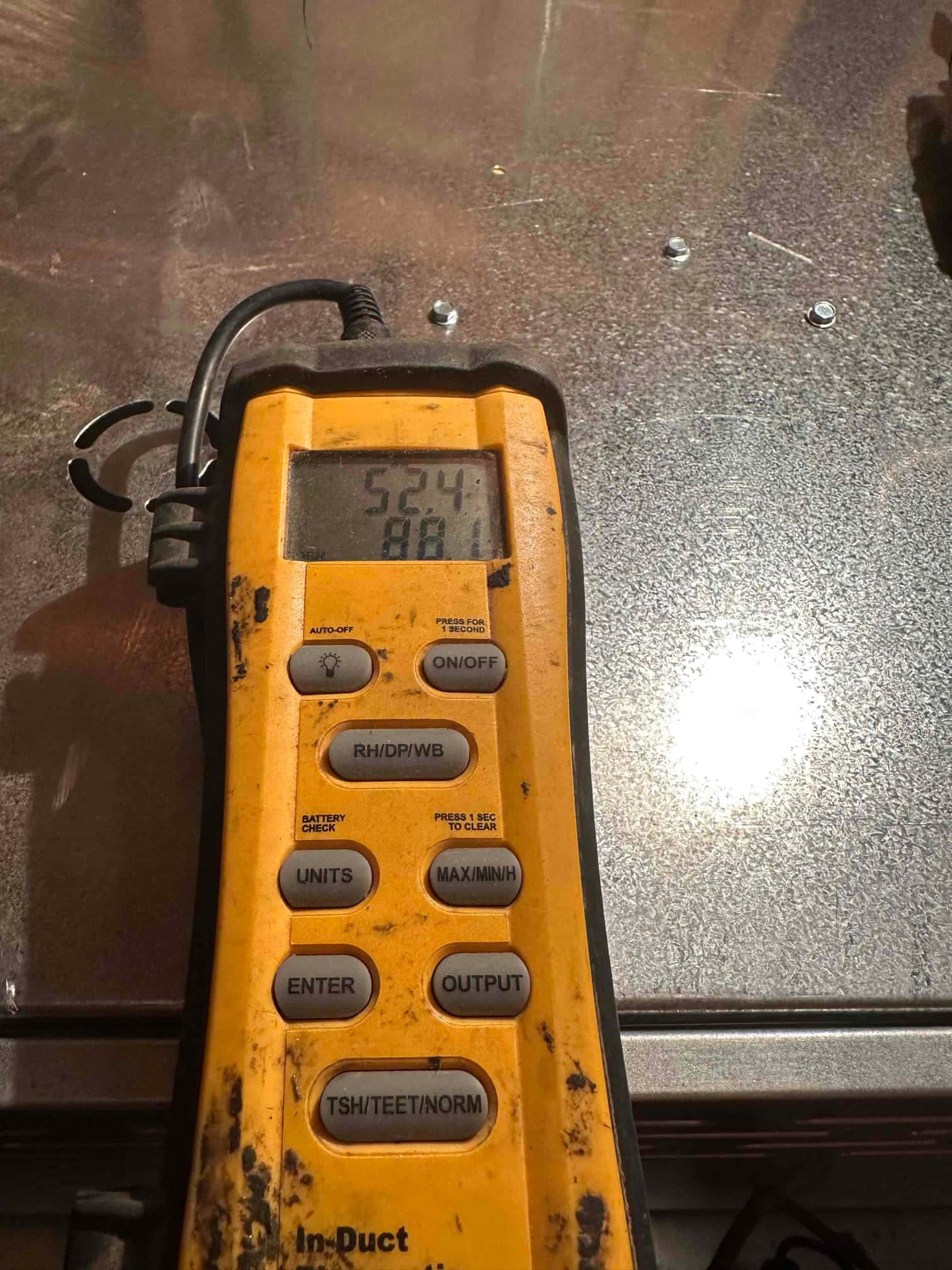 Digital thermometer displays 52.4 degrees Fahrenheit during supply air temperature check at the duct.