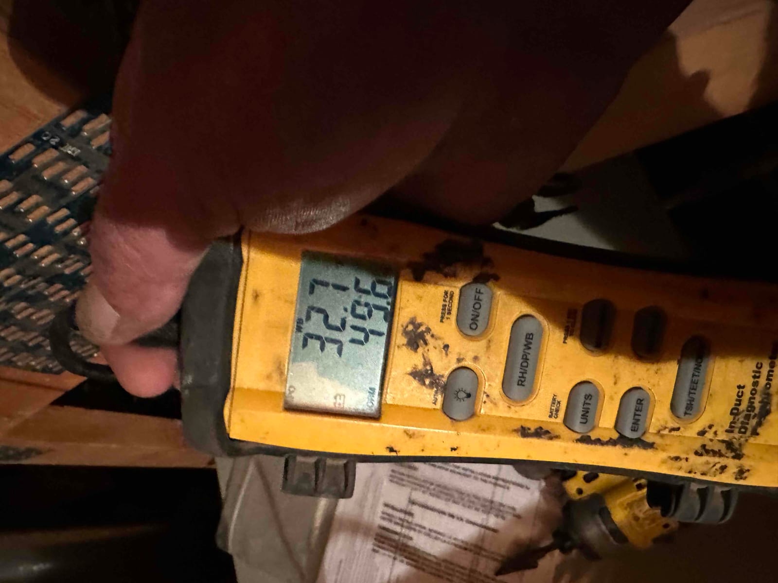 Digital thermometer displays 55.4°F while measuring air temperature during system startup checks in the ductwork.