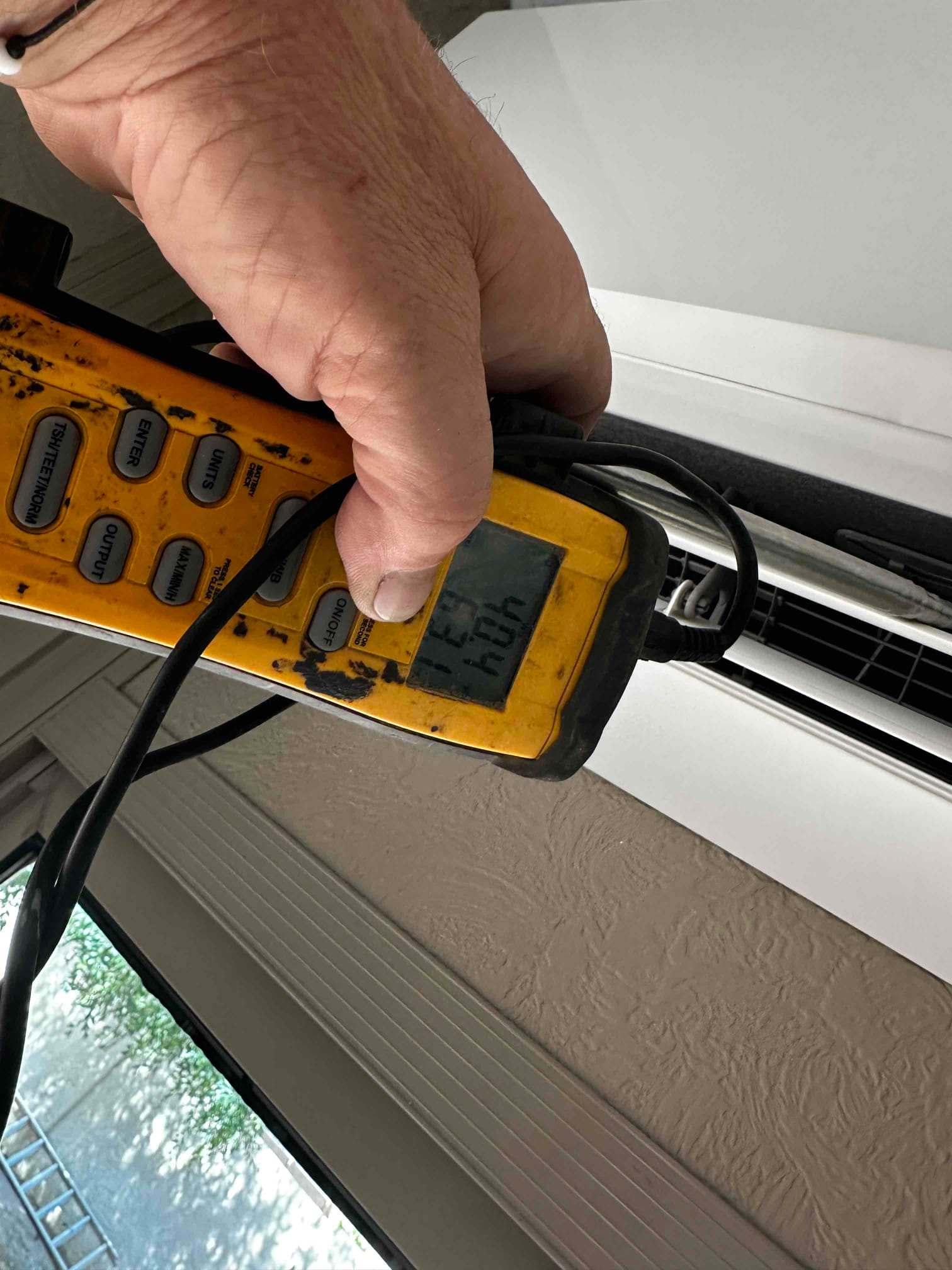 Digital thermometer probe at the wall-mounted indoor unit grille measures air temperature during mini-split commissioning.