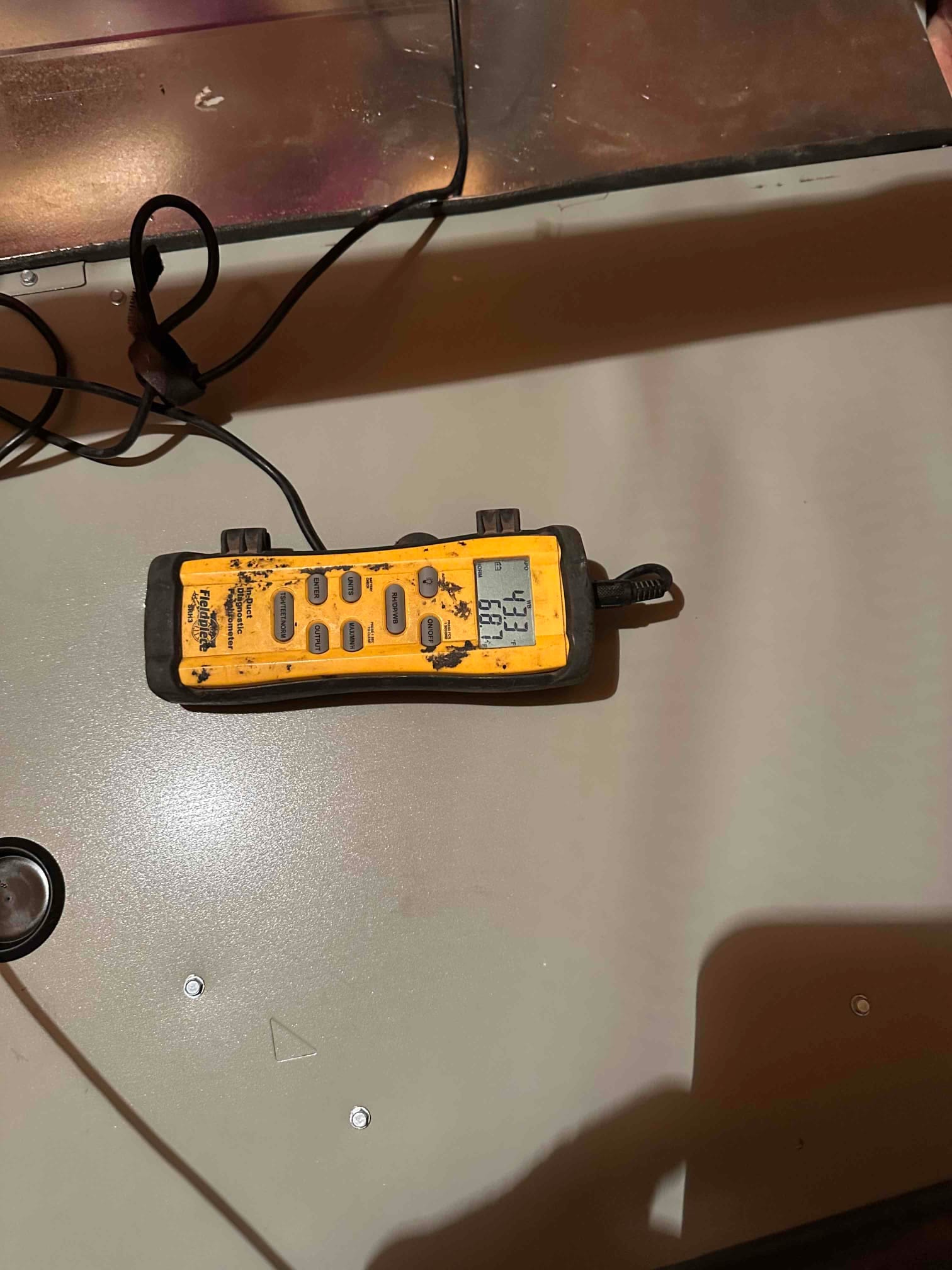 Digital thermometer rests on the air handler cabinet, displaying 59°F to document cooled supply air temperature.