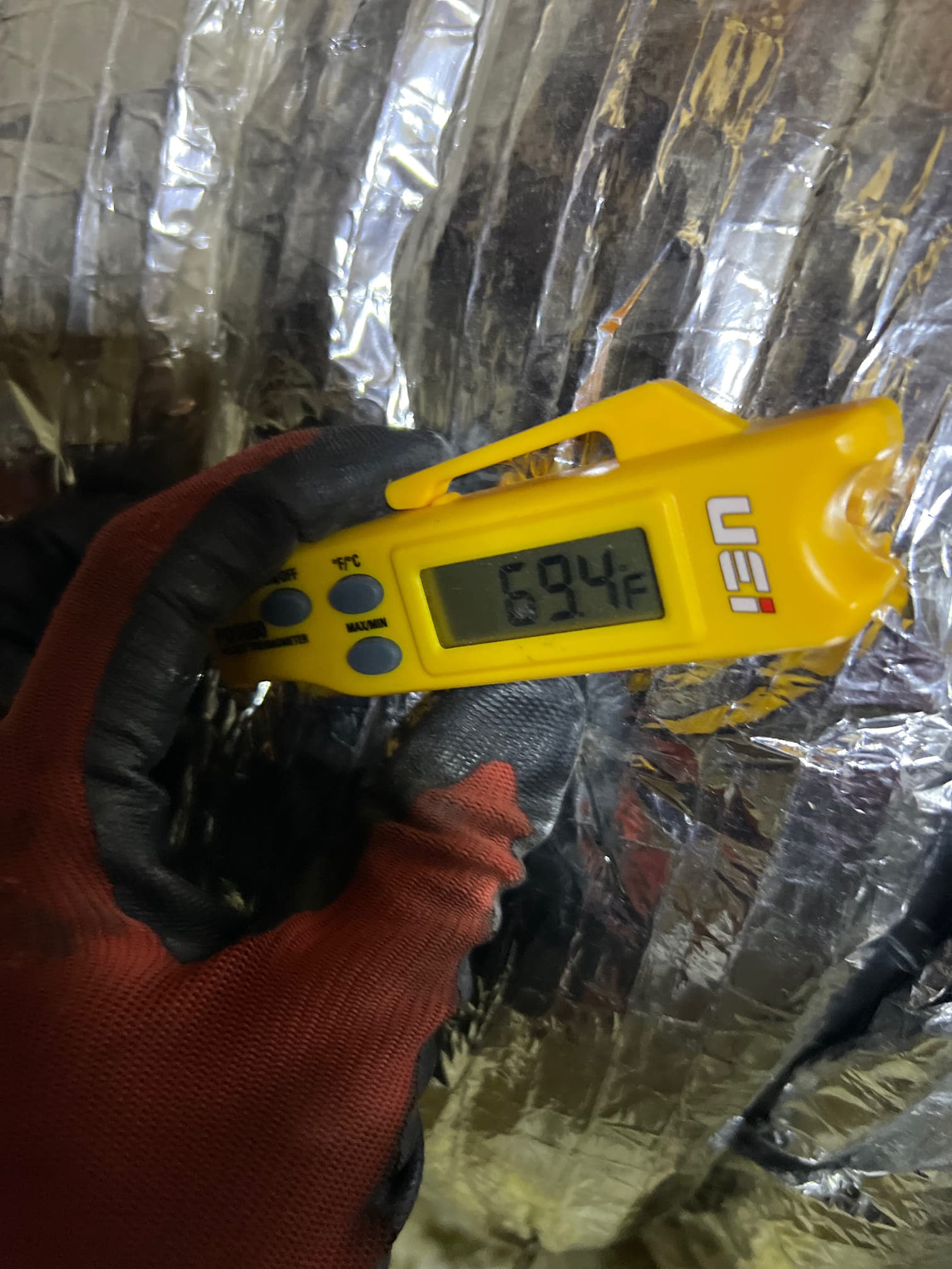 Digital thermometer shows 69.4°F while checking air temperature during HVAC commissioning.
