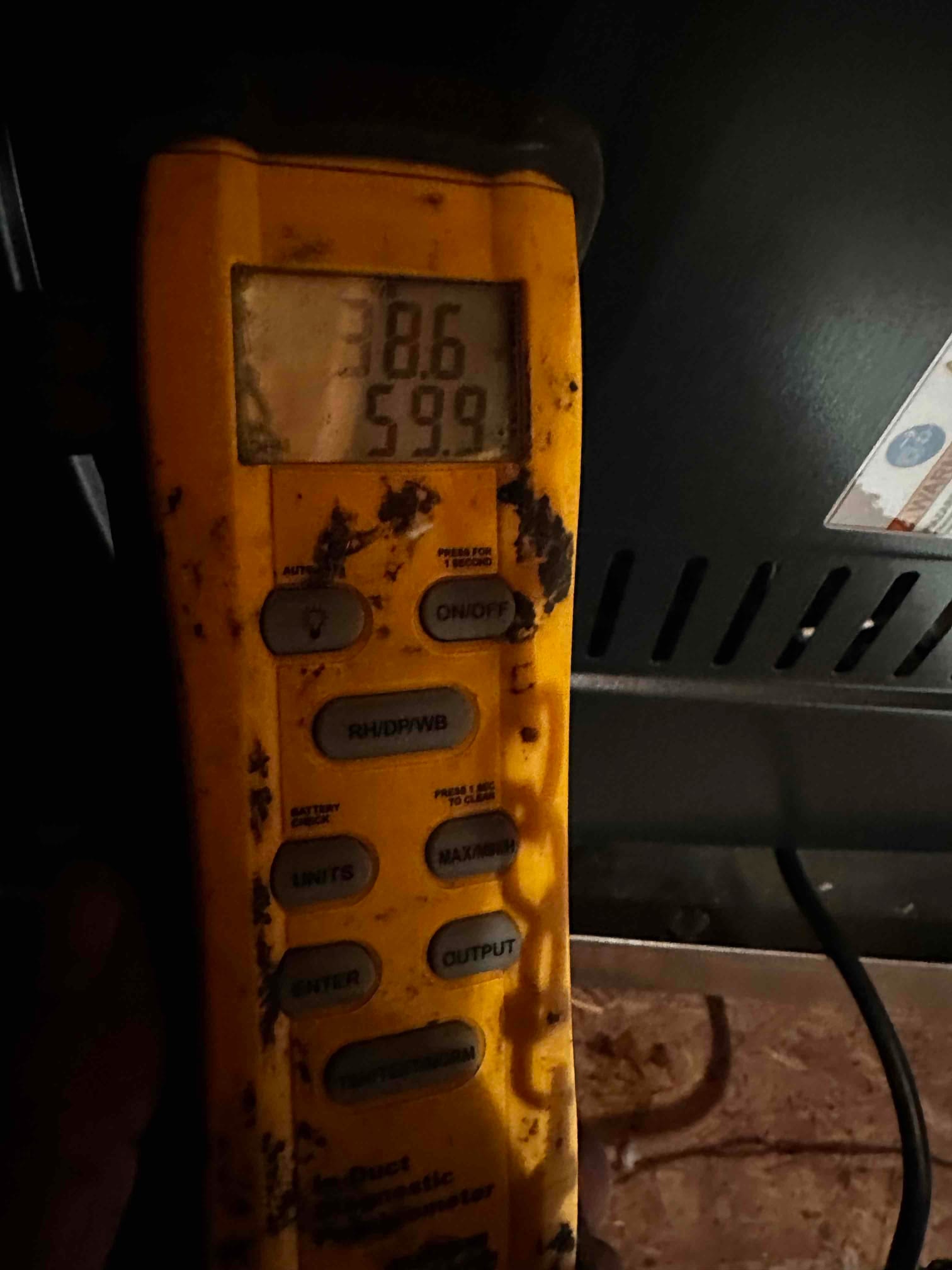 Digital thermometer shows air temperature readings of 38.6 and 59.9 degrees while checking the duct system during commissioning.