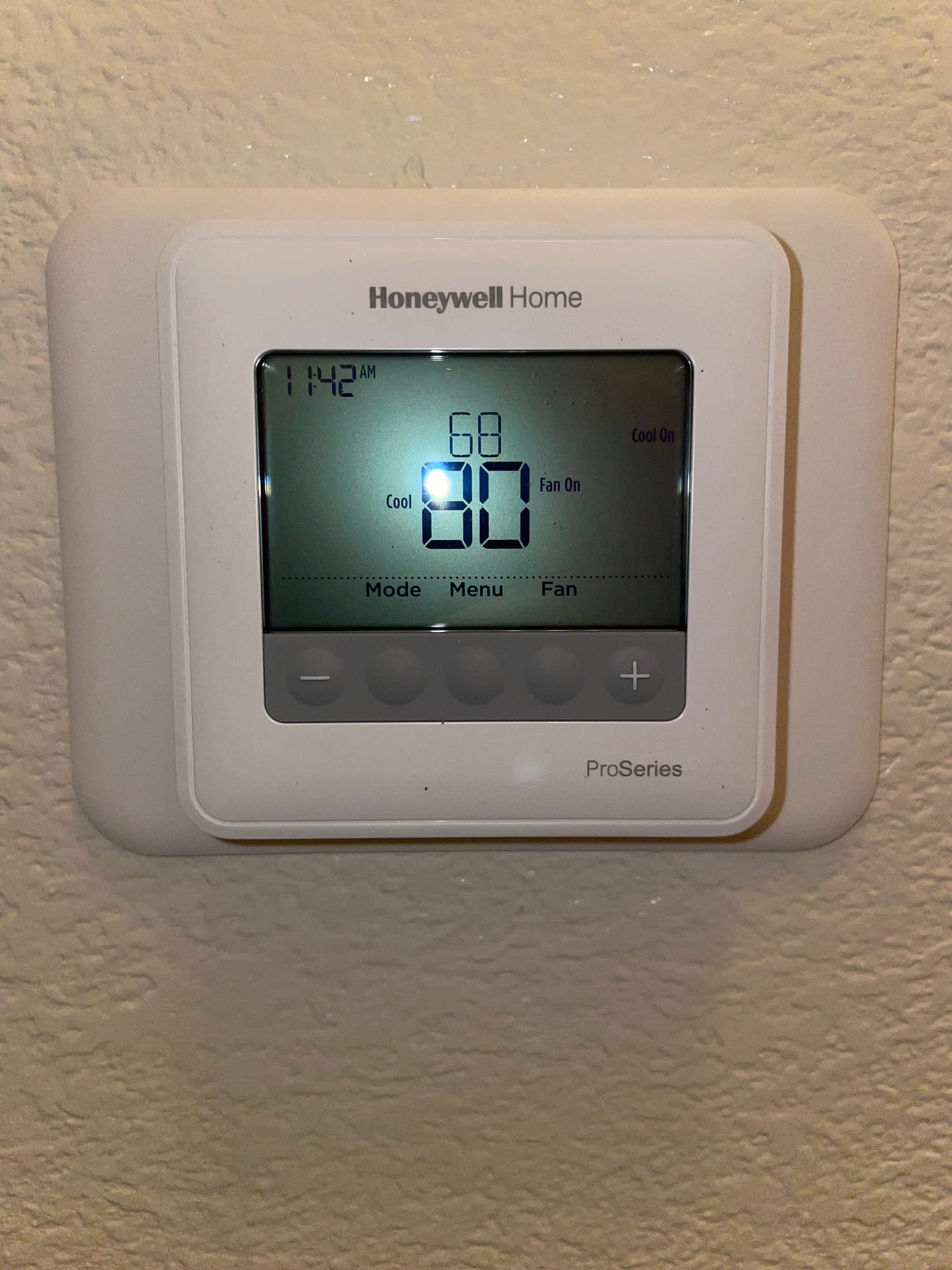 Digital thermostat mounted on interior wall displaying cooling mode with setpoint and fan status during system checkout.