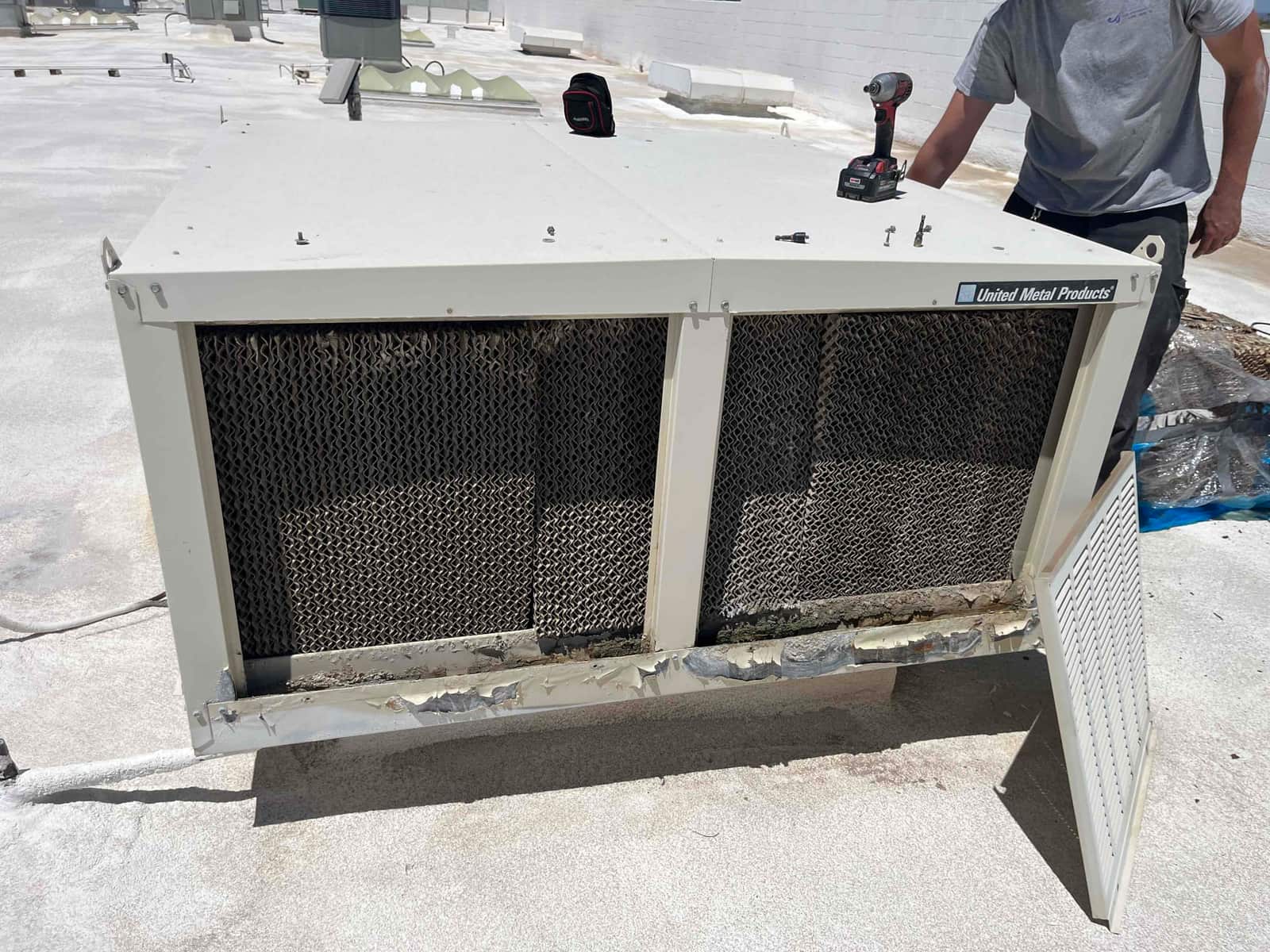 Evaporative cooler with the access panel open, showing worn cellulose media pads and corrosion along the lower housing.
