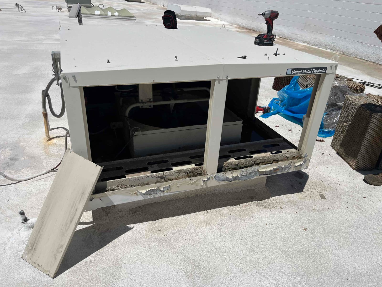Evaporative cooler cabinet opened on a rooftop, with media pad panel removed to access the internal water distribution tray.