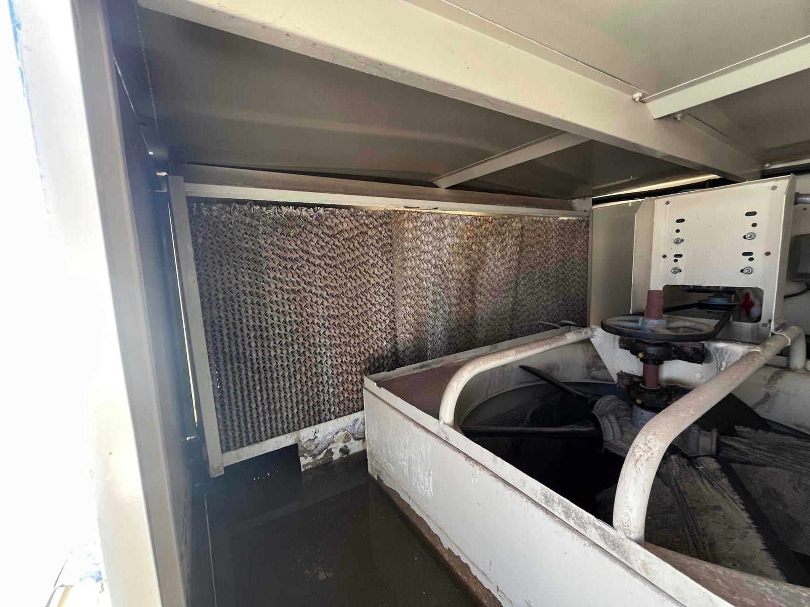 Evaporative cooler interior showing the media pad behind the distribution tray and fan housing, with mineral buildup visible on the pad.