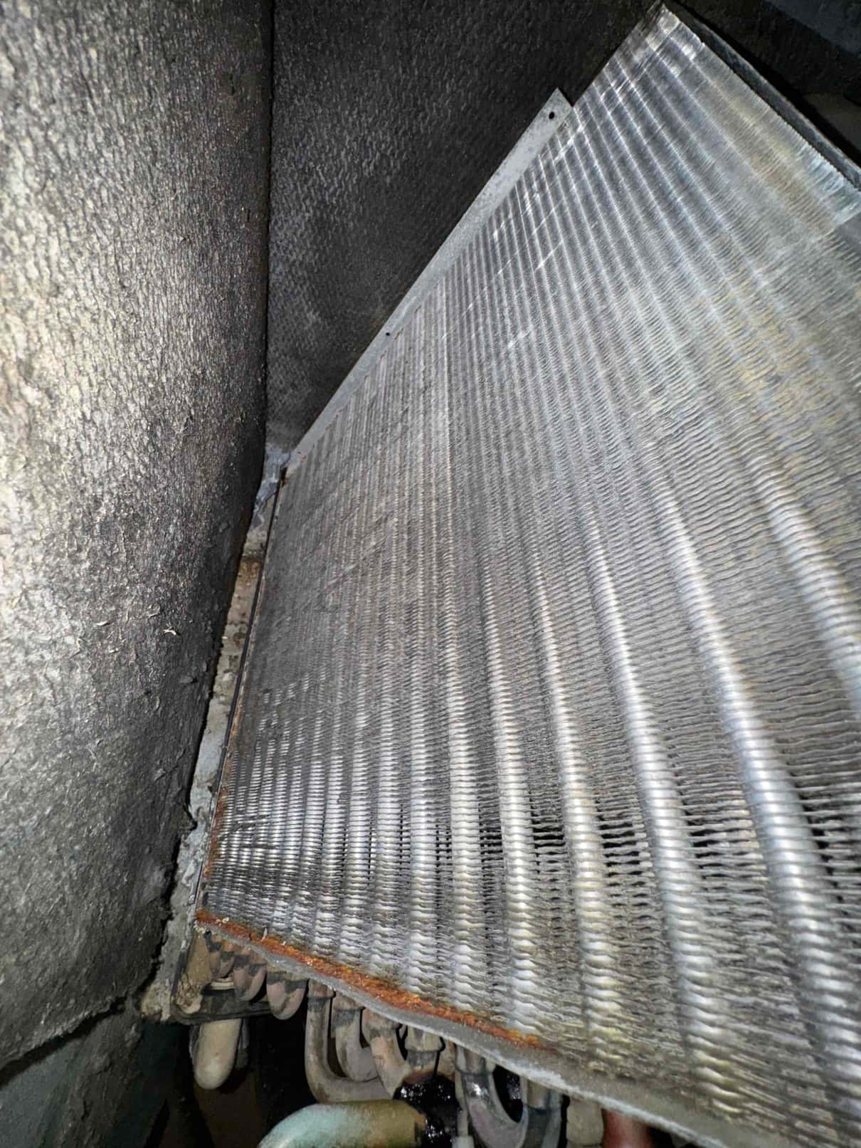 Evaporator coil assembly inside the air handler, showing dusty fins and rust along the bottom edge of the frame.