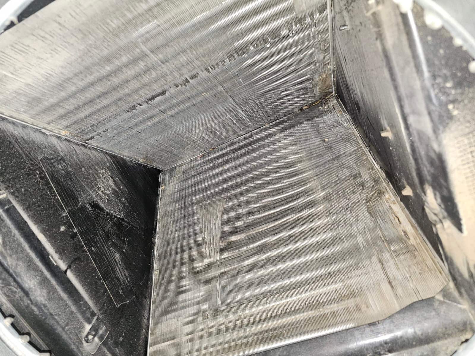 Evaporator A-coil inside air handler, showing fin surfaces with accumulated dust and moisture streaks along the panels.