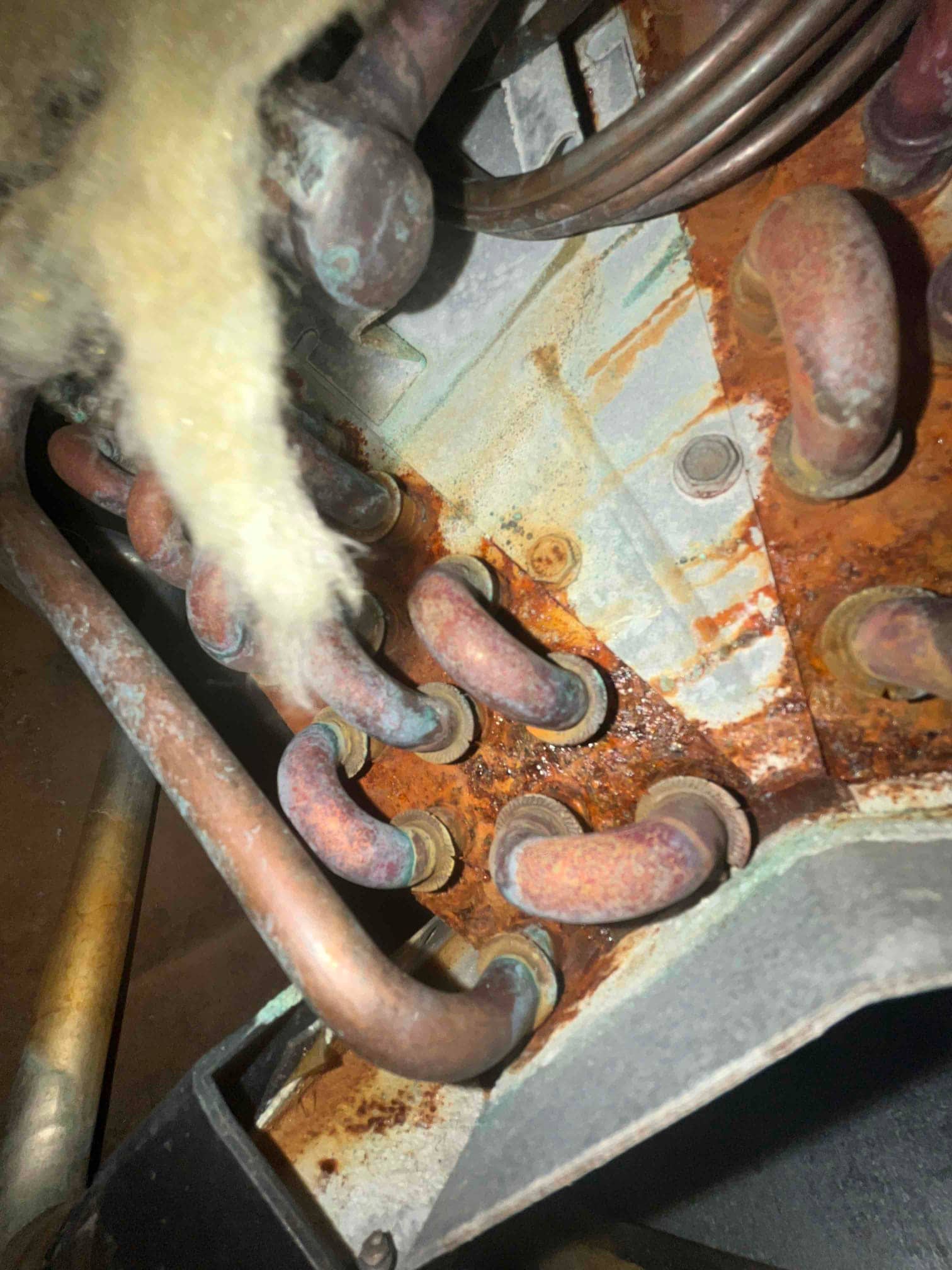 Evaporator coil manifold with multiple copper U-bends showing heavy rust and corrosion on the drain pan area.