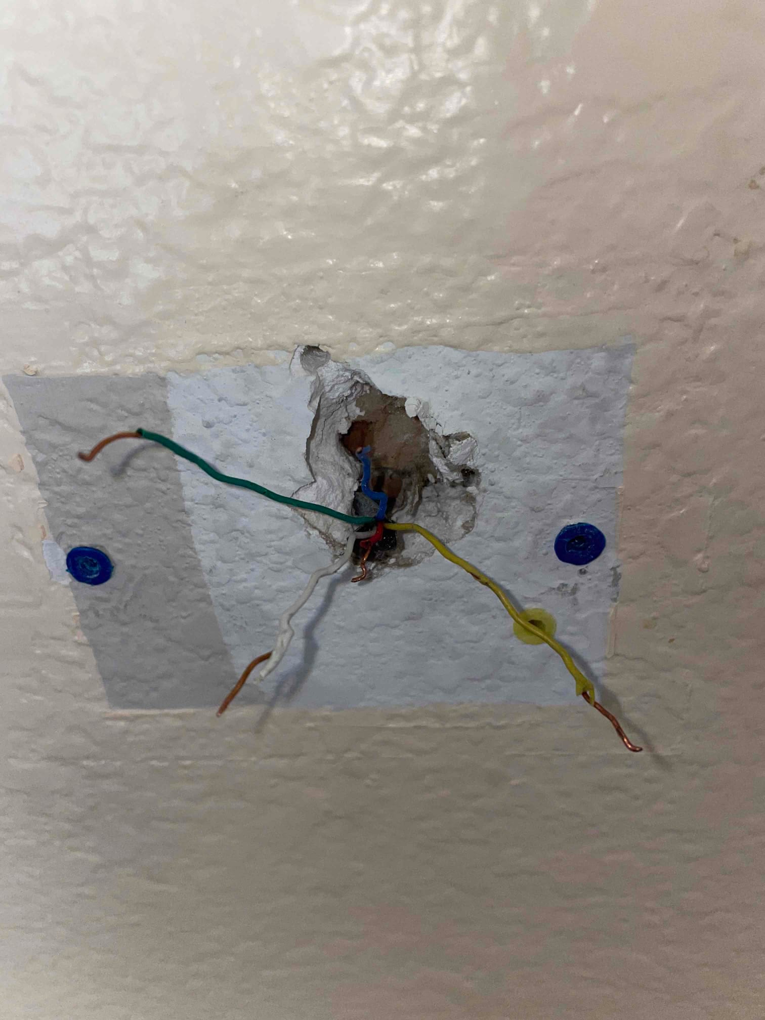Exposed low-voltage control wires extend from a wall opening, with surrounding patch material and two visible wall anchors.